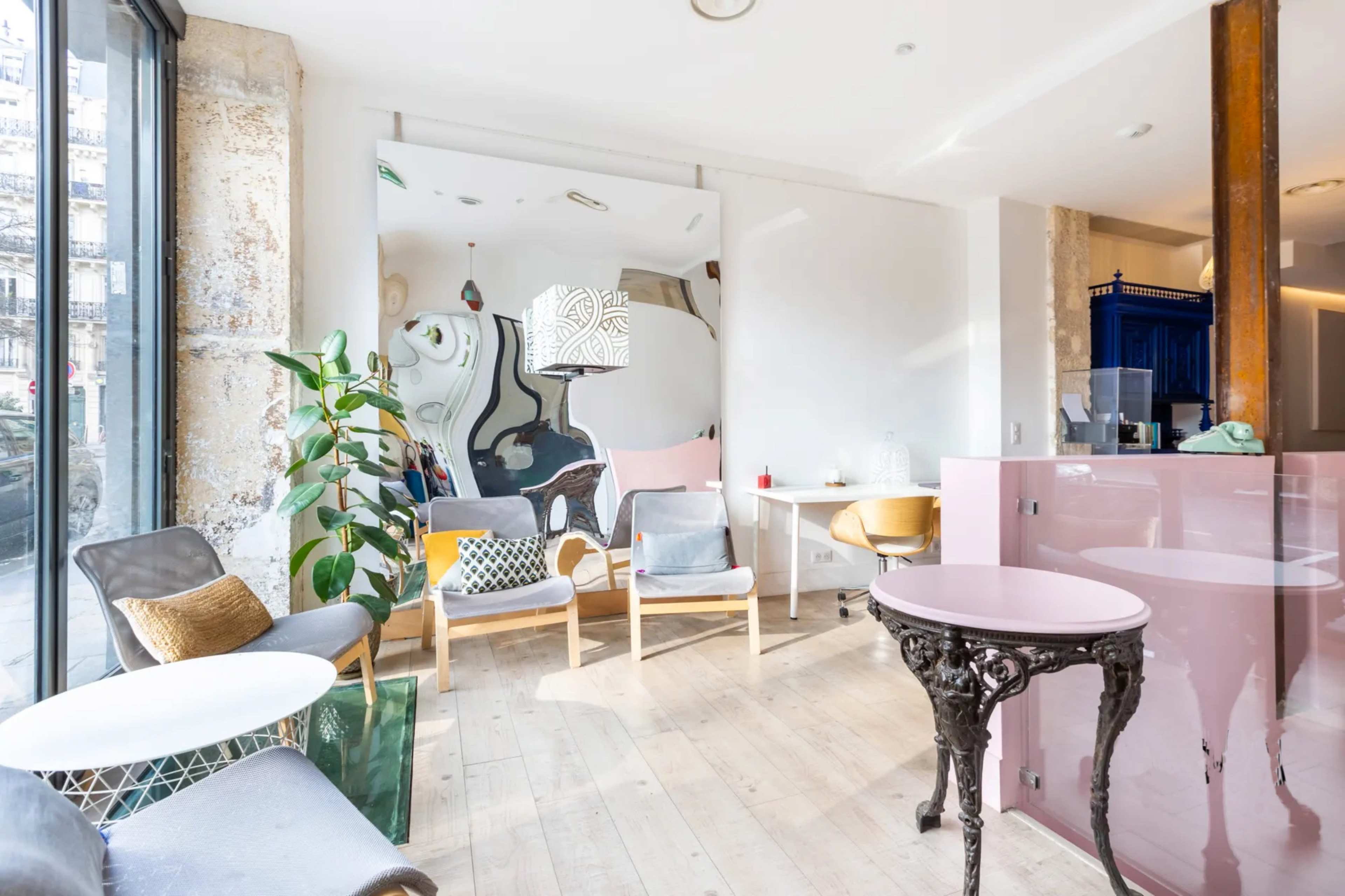 A modern interior space with wooden flooring, a mix of seating options, large windows, and a mirrored wall.