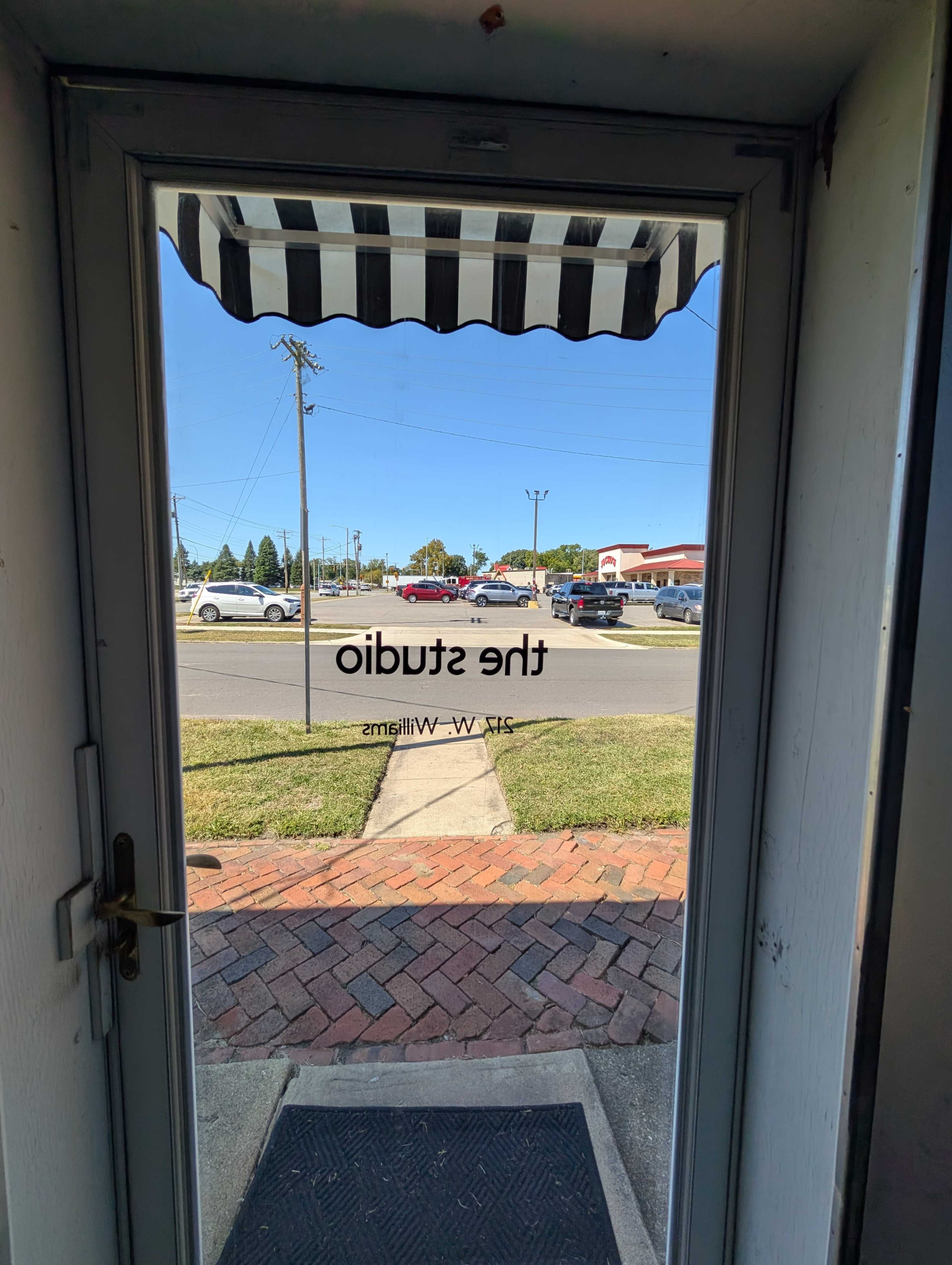 The image shows a doorway with a sign reading "the studio" visible on the glass, looking out onto a street with parked cars and clear blue skies.