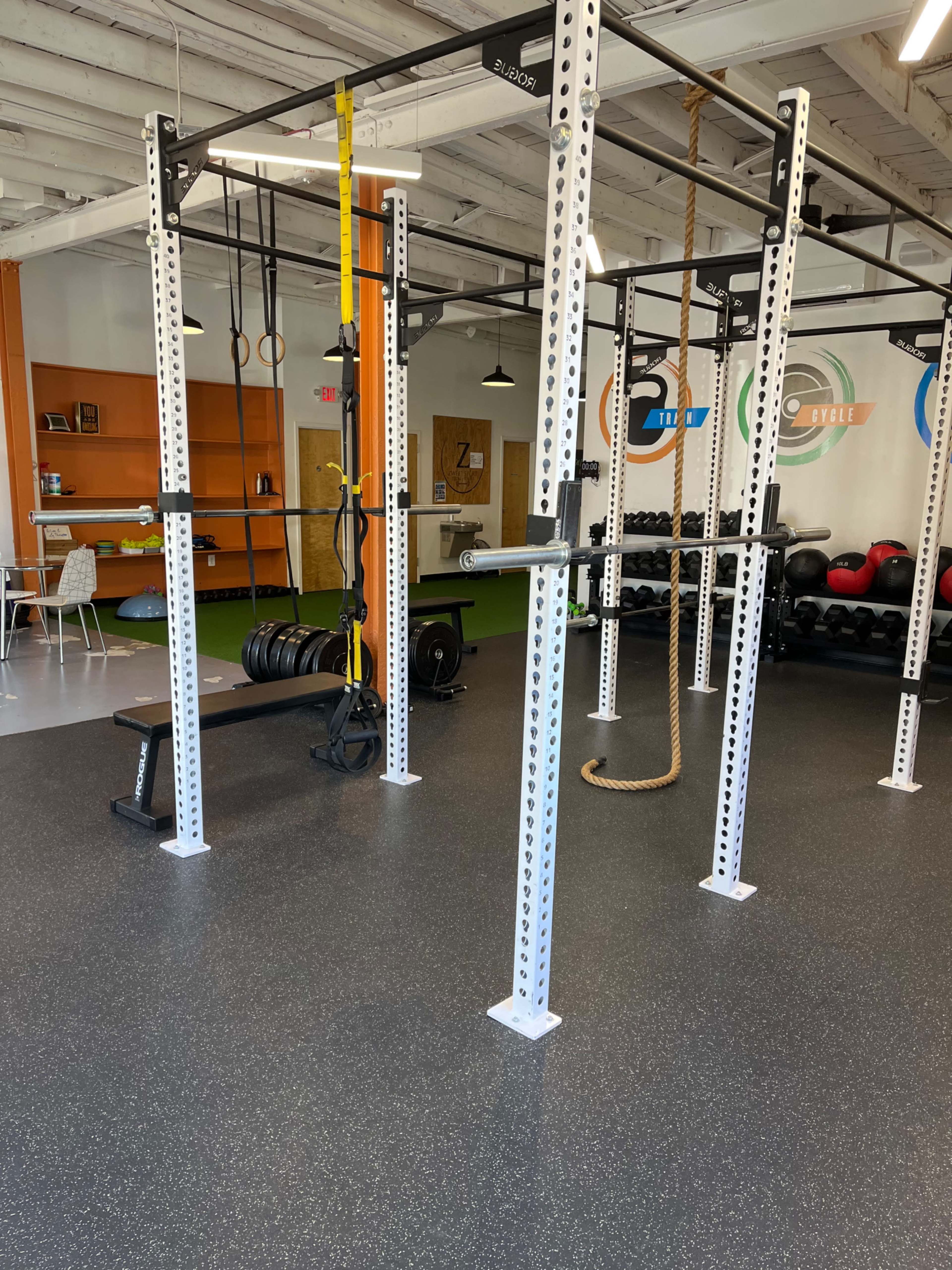 A gym space featuring a weightlifting bench, a pull-up rig, exercise equipment, and a green turf area.
