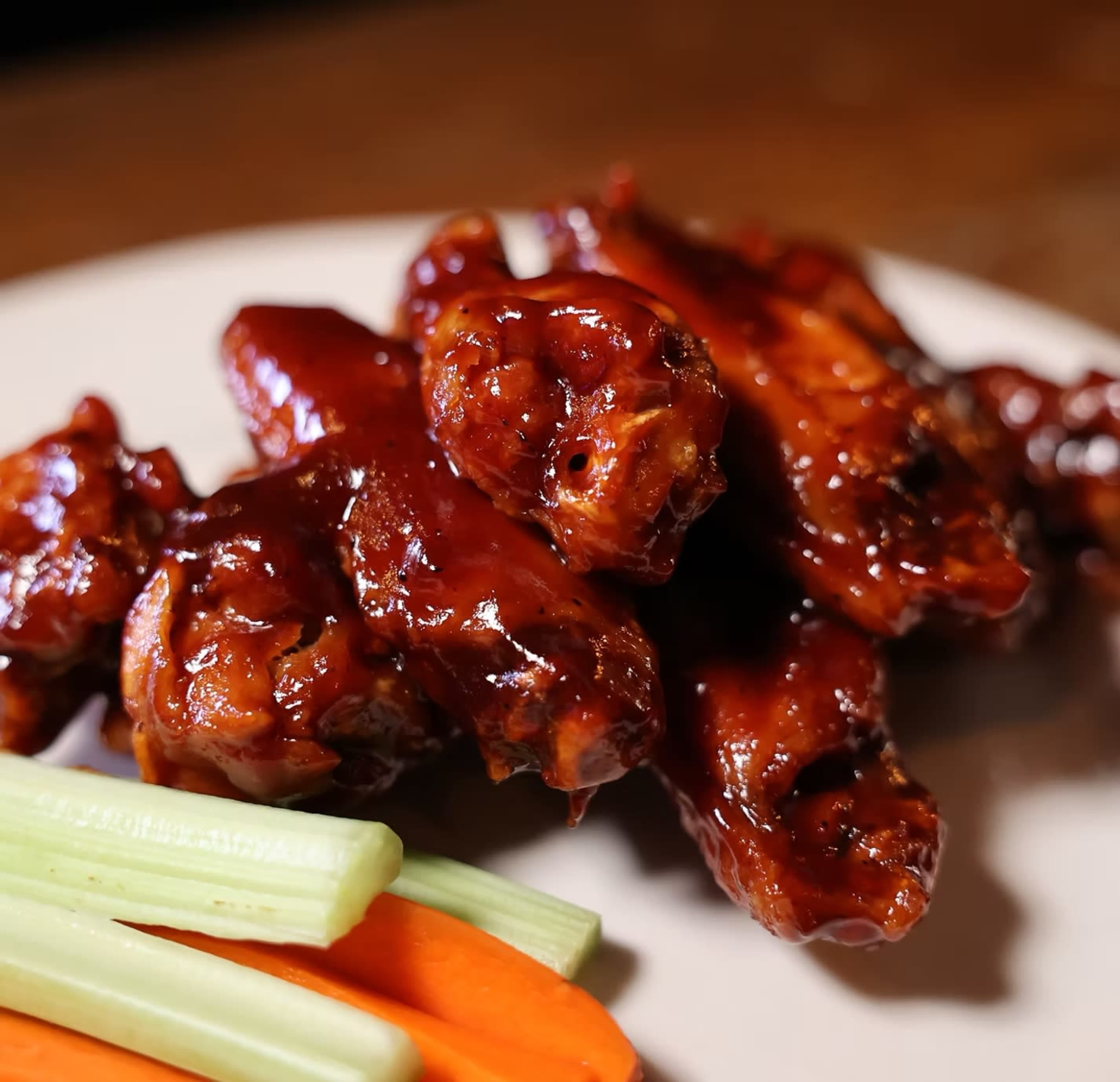 A plate of glazed chicken wings is accompanied by celery and carrot sticks.