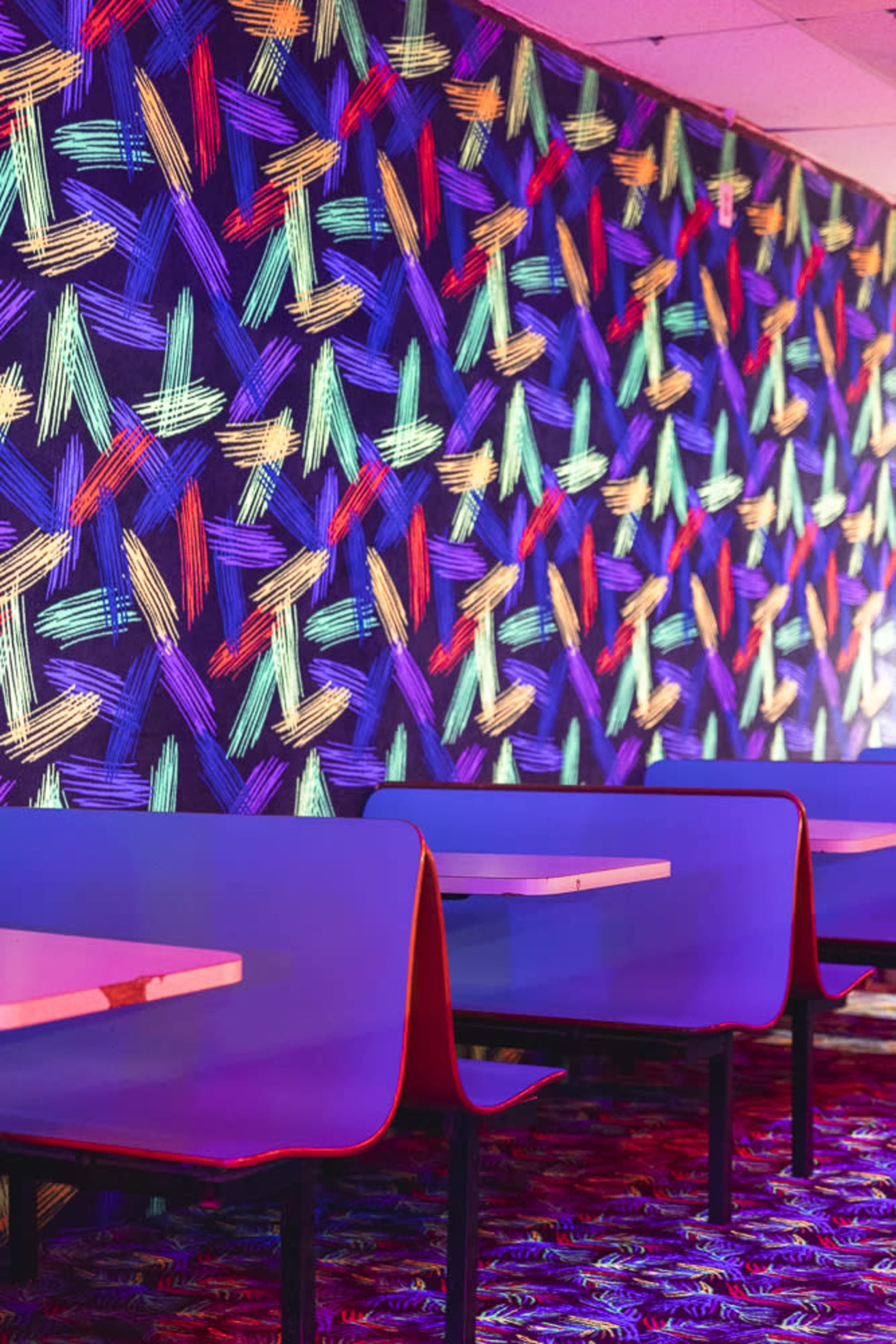 The image shows a vibrant dining area with brightly patterned wallpaper and simple tables and chairs.