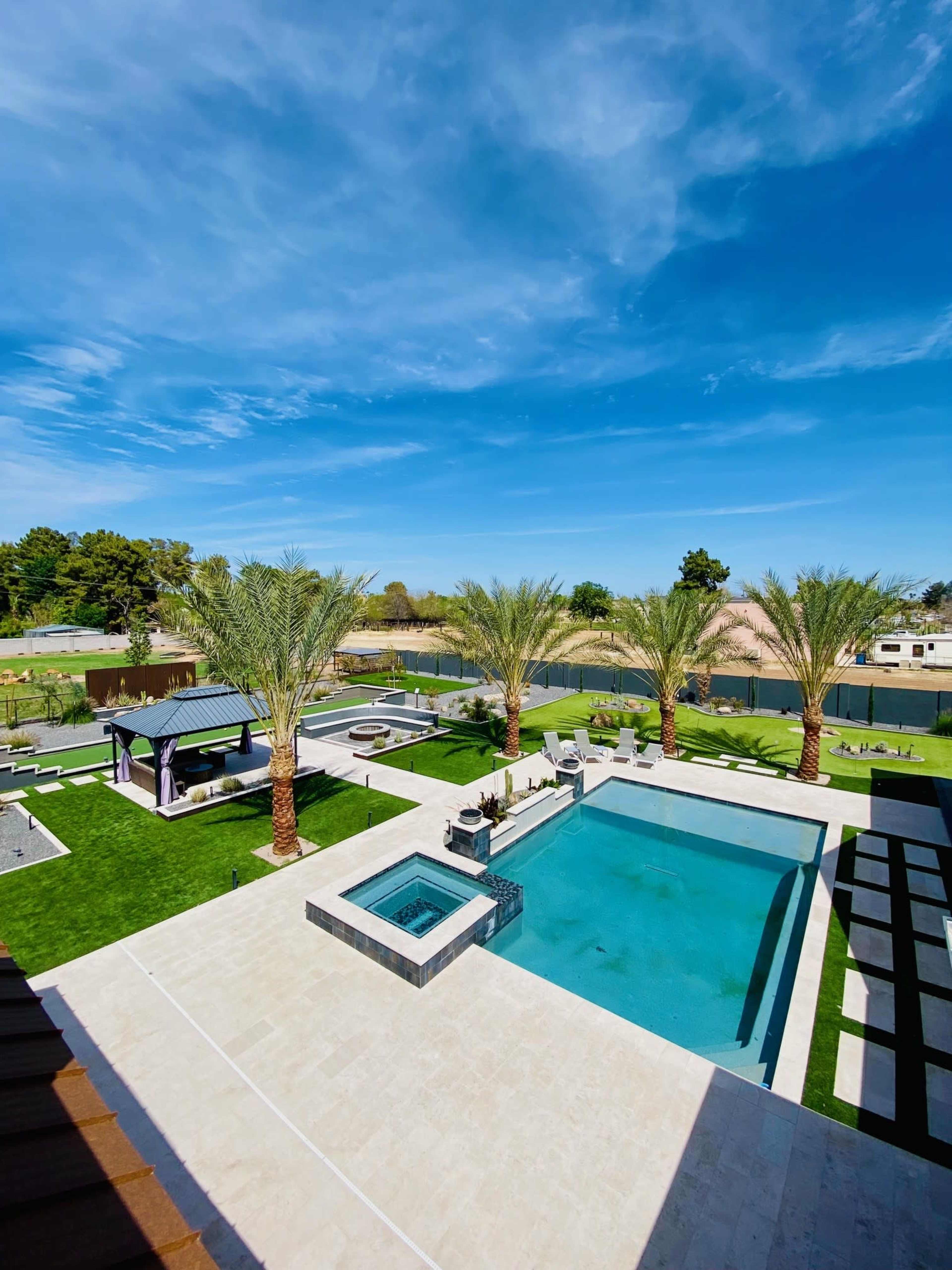 The image shows a spacious outdoor area featuring a swimming pool, a spa, and palm trees, with lounge seating and landscaping.