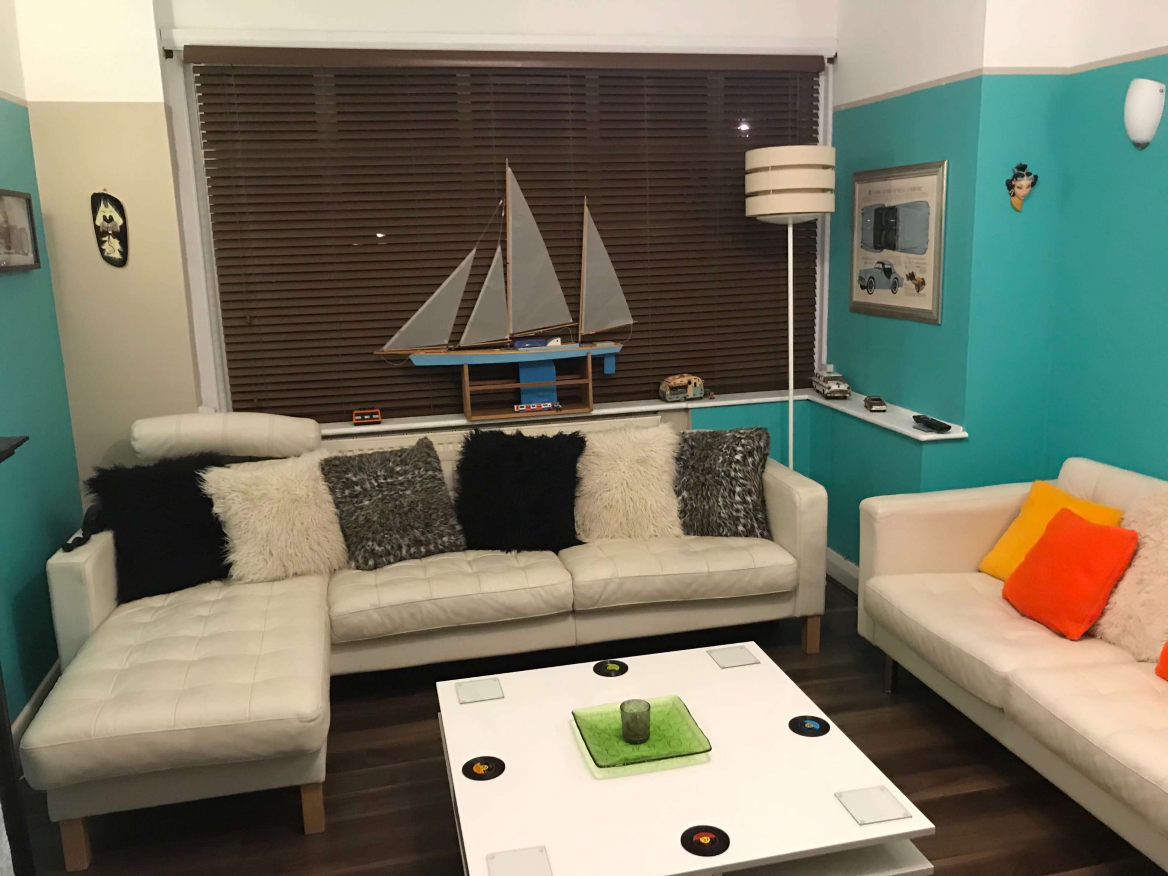 The room features a modern seating area with a white leather sectional and chairs, a coffee table, and a model sailboat displayed on the window ledge.