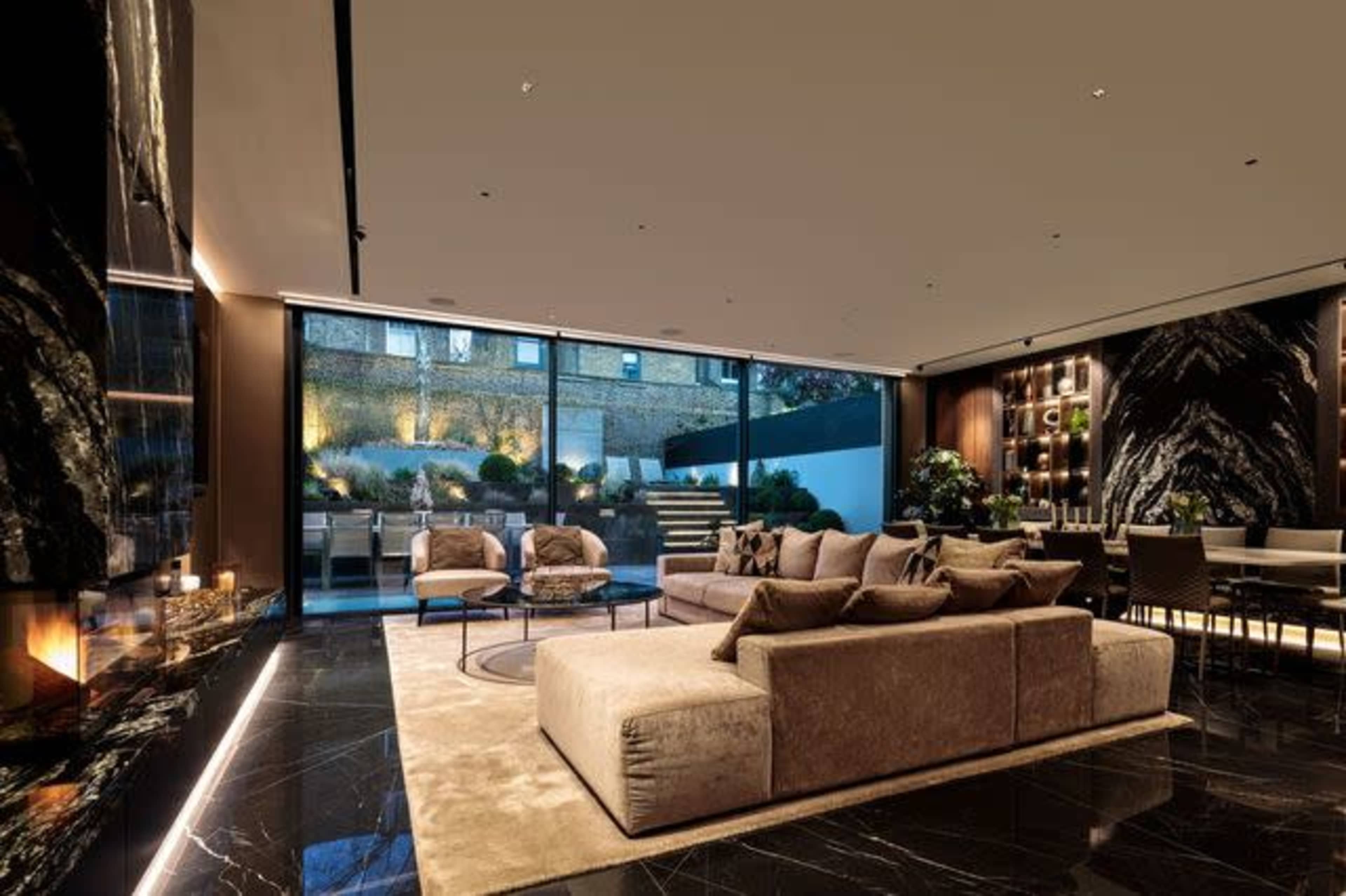 A modern living room with a large sectional sofa, a round coffee table, and floor-to-ceiling windows overlooking an outdoor garden space.