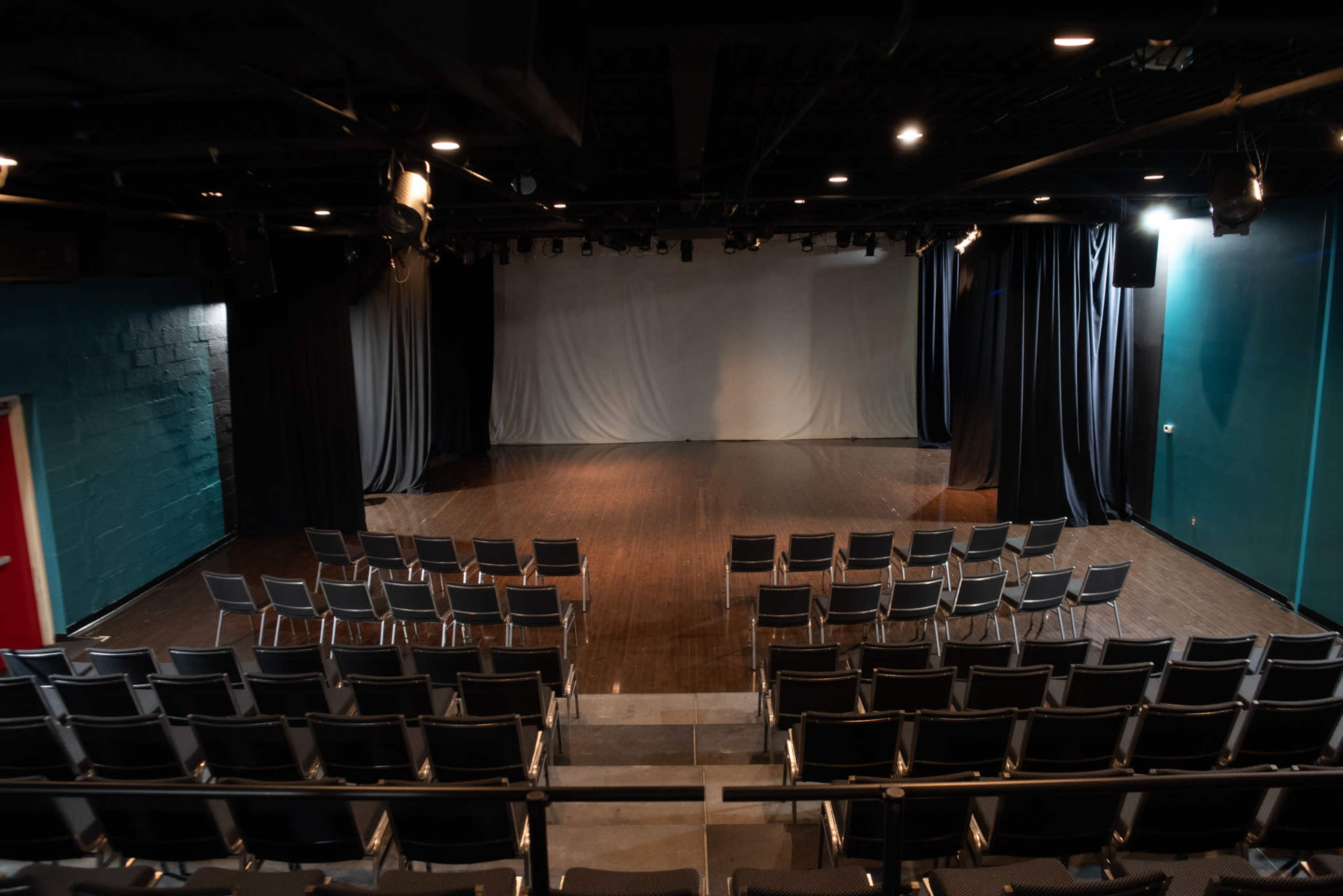 A small theater with rows of black chairs facing a stage that has a plain white backdrop.