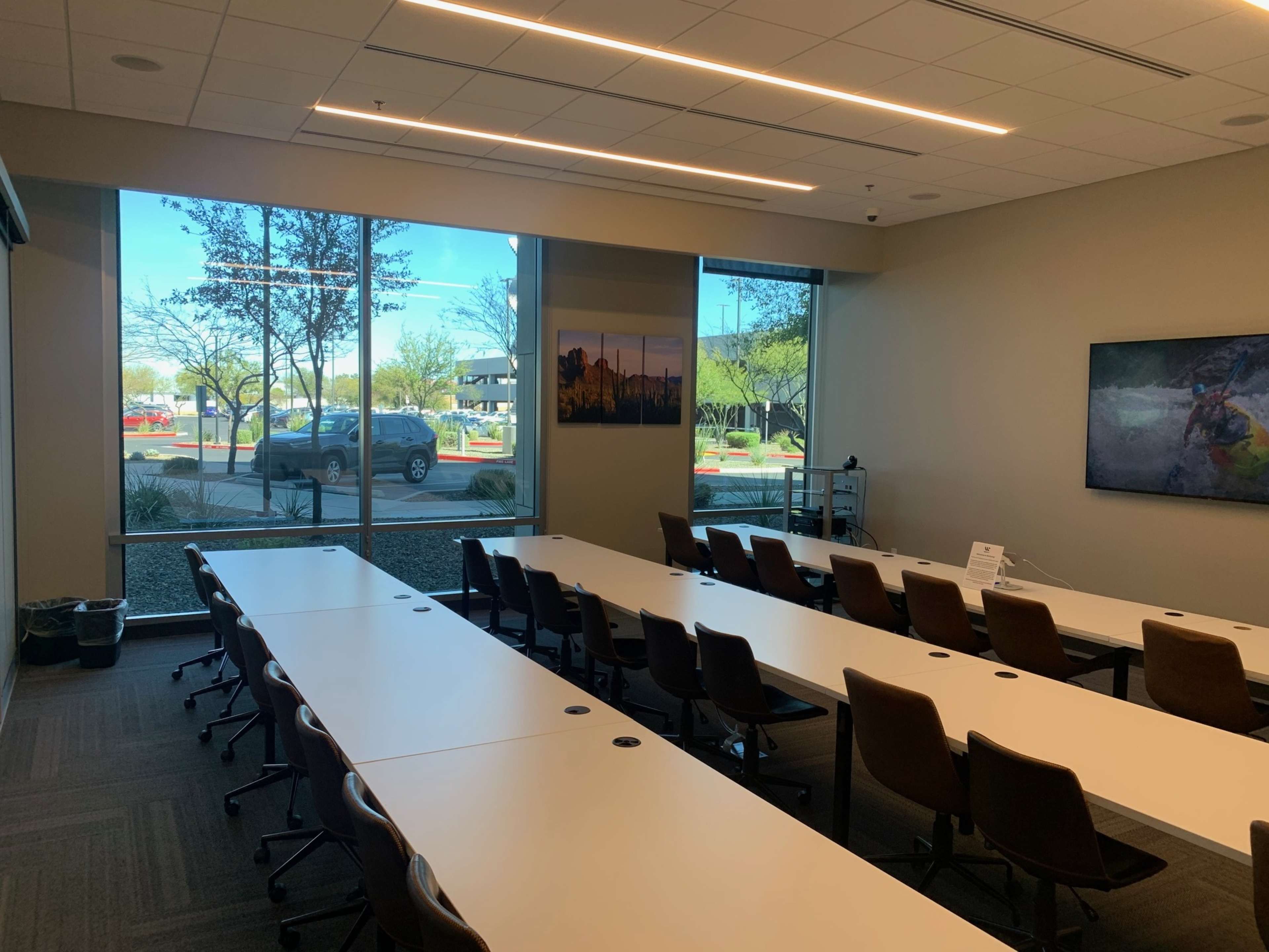 The image shows a conference room with multiple long tables arranged for a meeting, and large windows providing a view of the outside.
