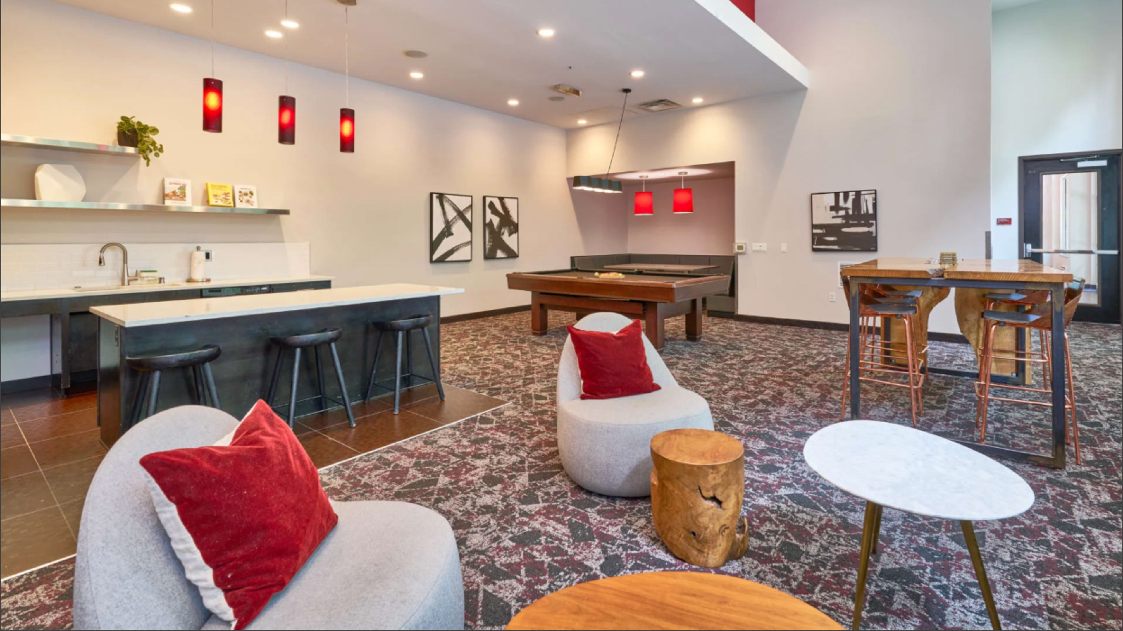 The image shows a modern communal lounge with a kitchen area, seating arrangements, a pool table, and decorative lighting.