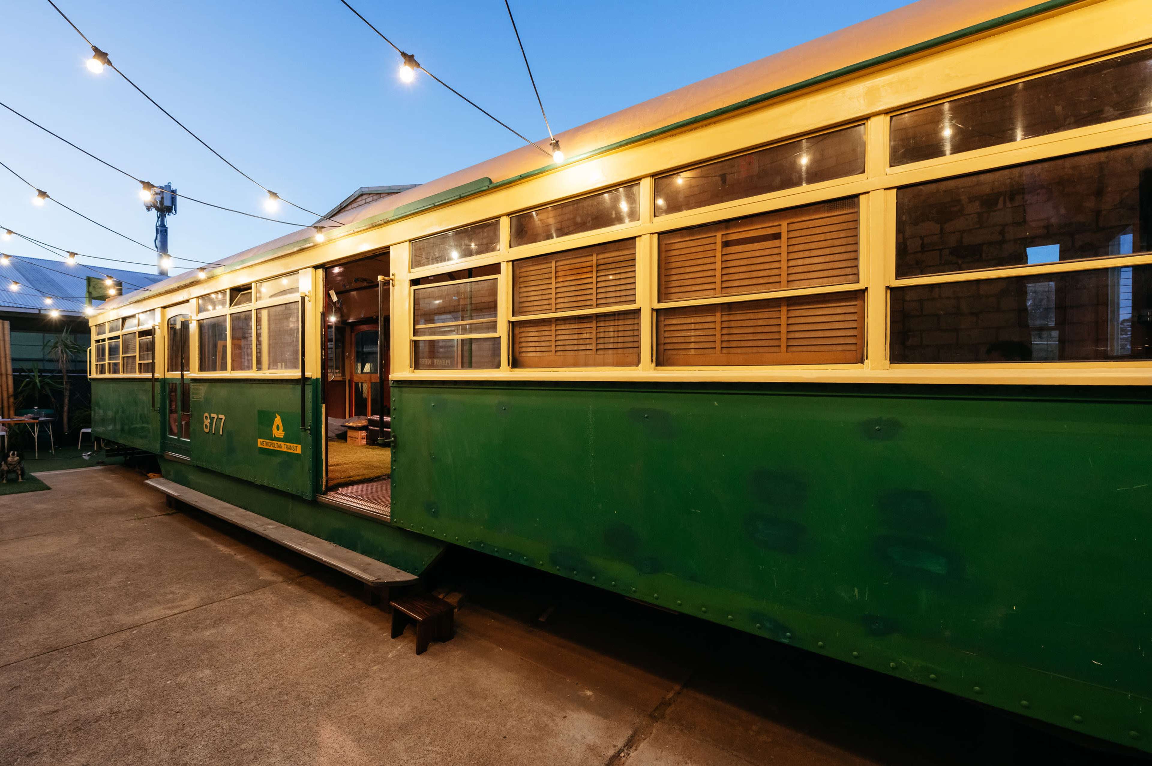 A vintage green tram is parked on a concrete surface, with string lights illuminating the area around it.