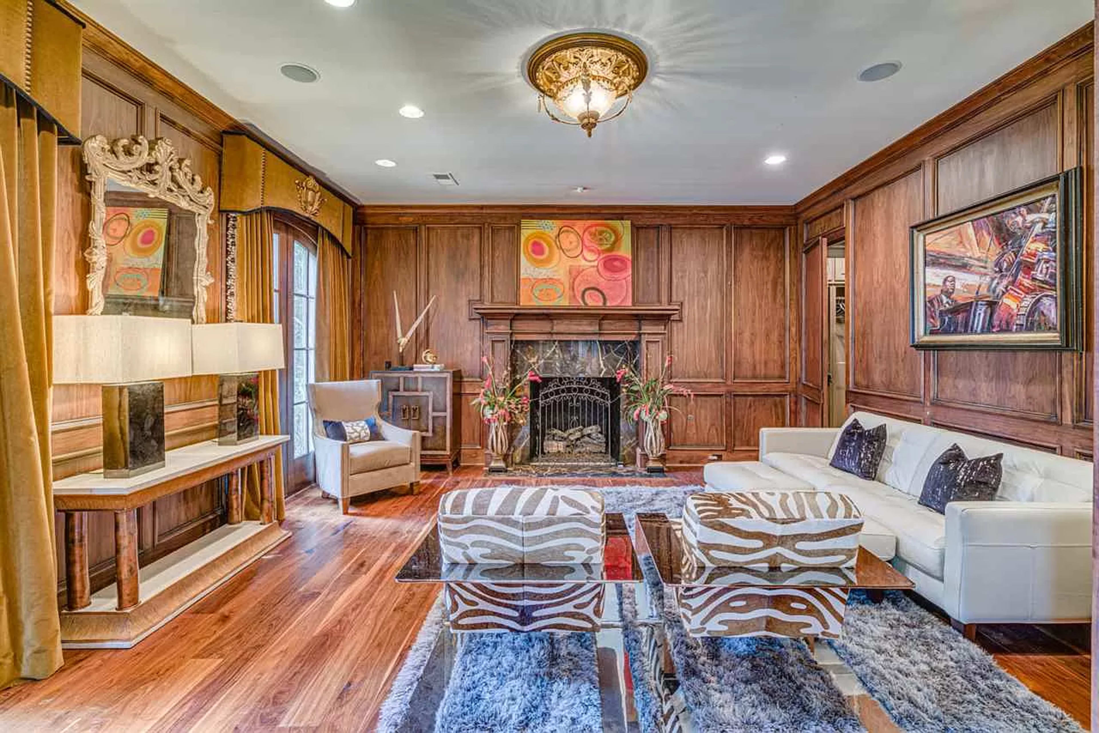 A polished living room with wooden paneling, a fireplace, and a mix of modern and traditional furniture, including a white sofa and zebra-striped chairs.
