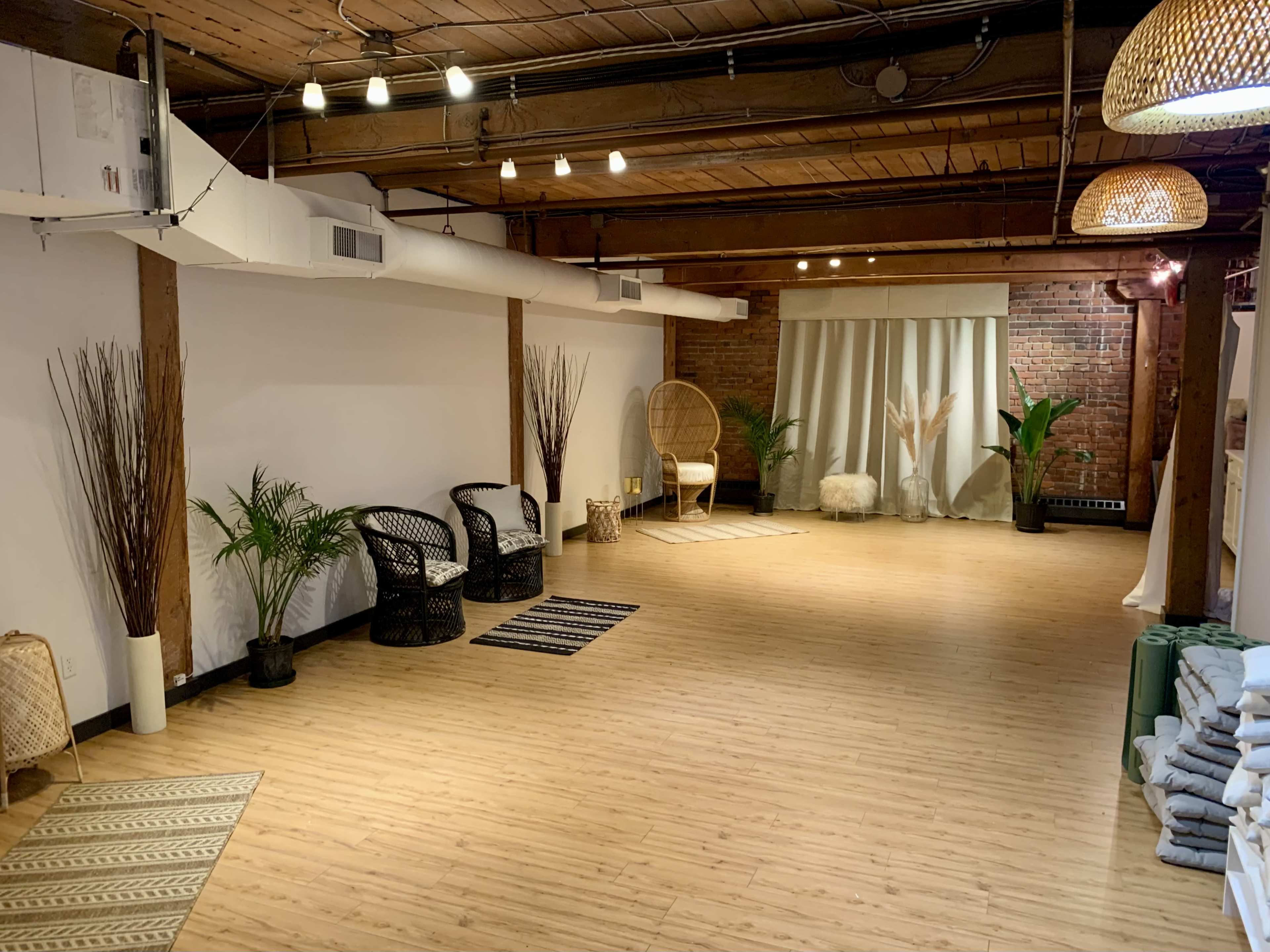 A spacious, well-lit room with wooden beams, featuring minimalist decor, plants, seating areas, and a soft color palette.