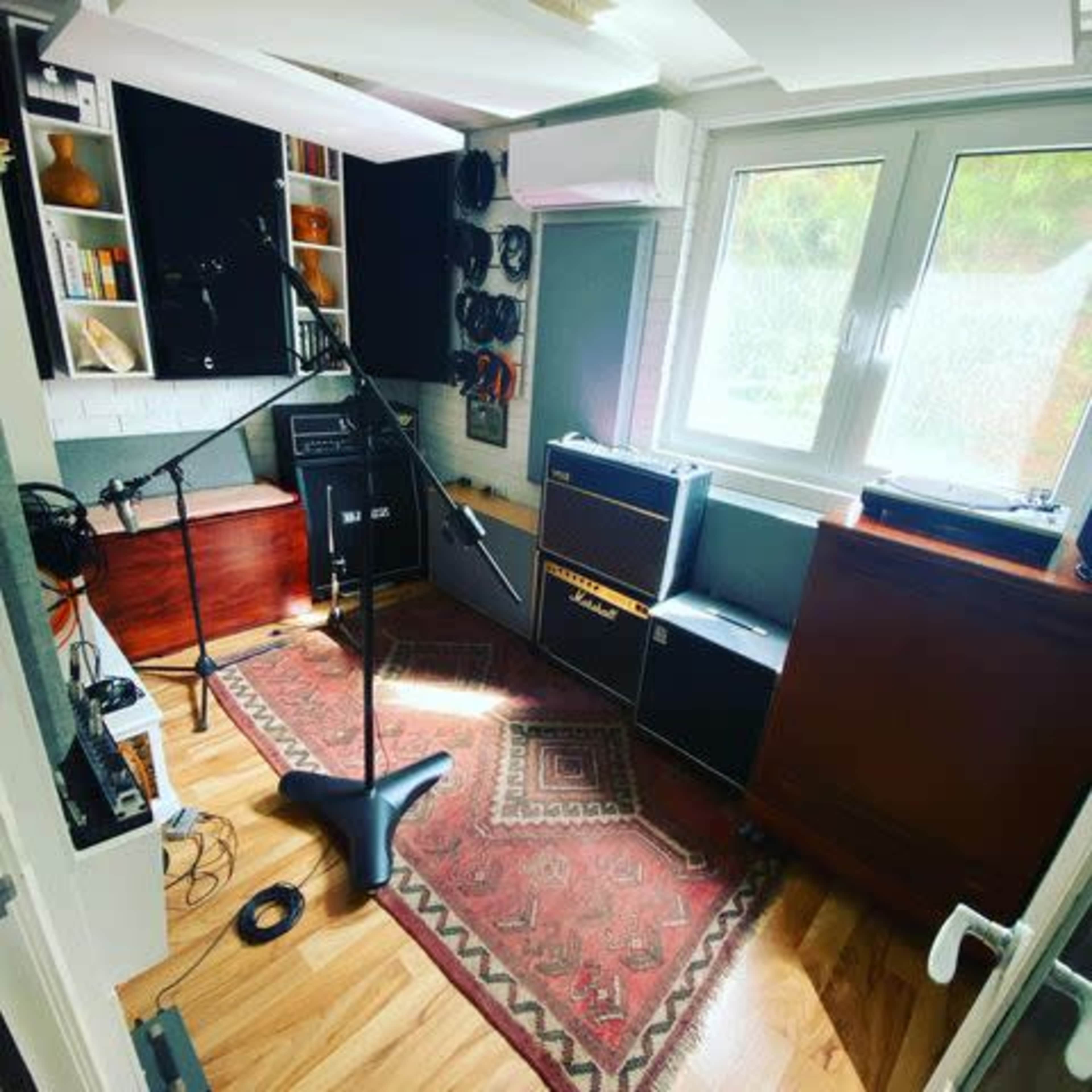 A small music studio equipped with amplifiers, microphones, and a rug on the wooden floor.