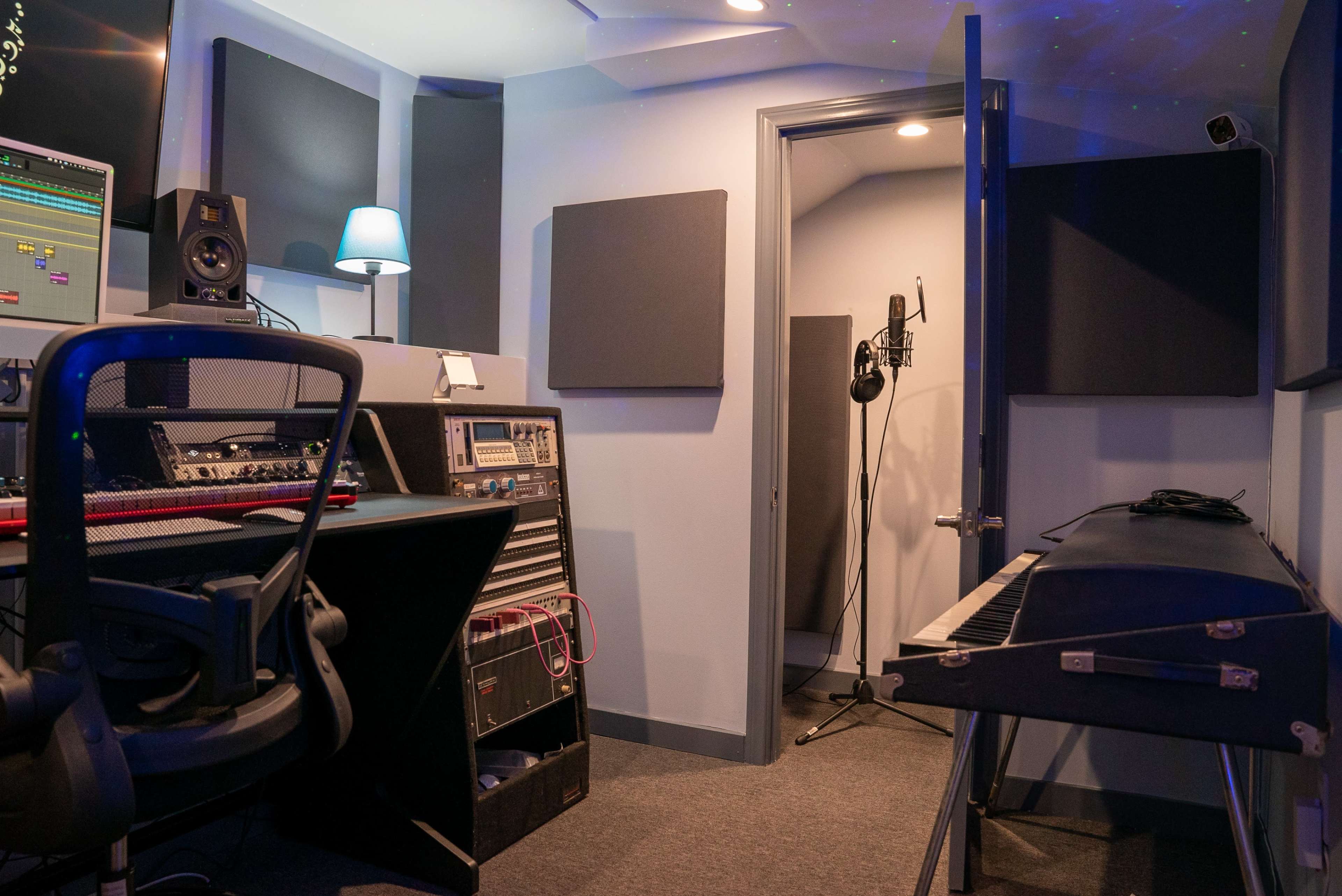 The image shows a small music studio with recording equipment, a keyboard, and a microphone set up in a corner.