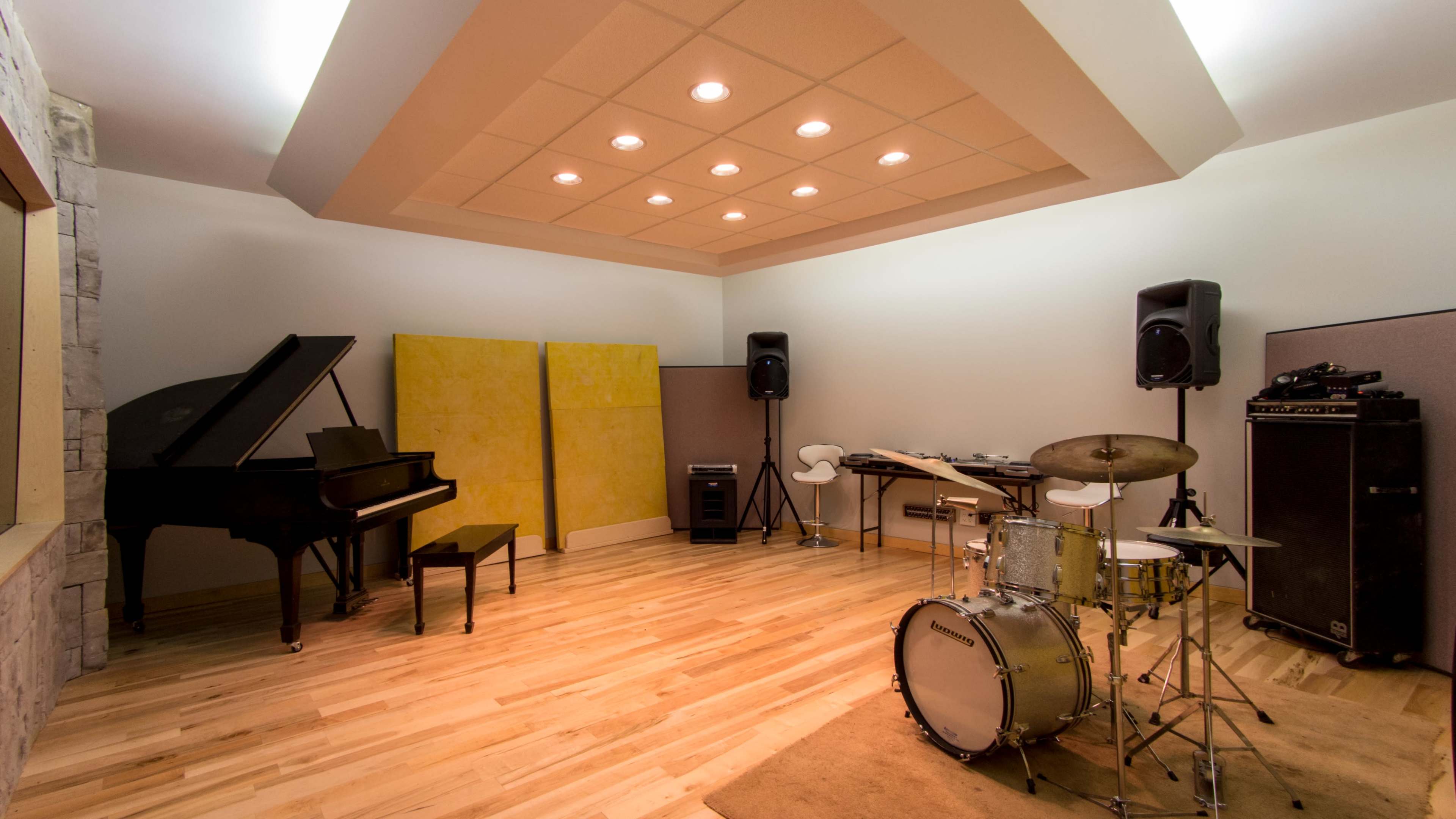 The image shows a music studio with a grand piano, a drum set, amplifiers, and soundproof wall panels.