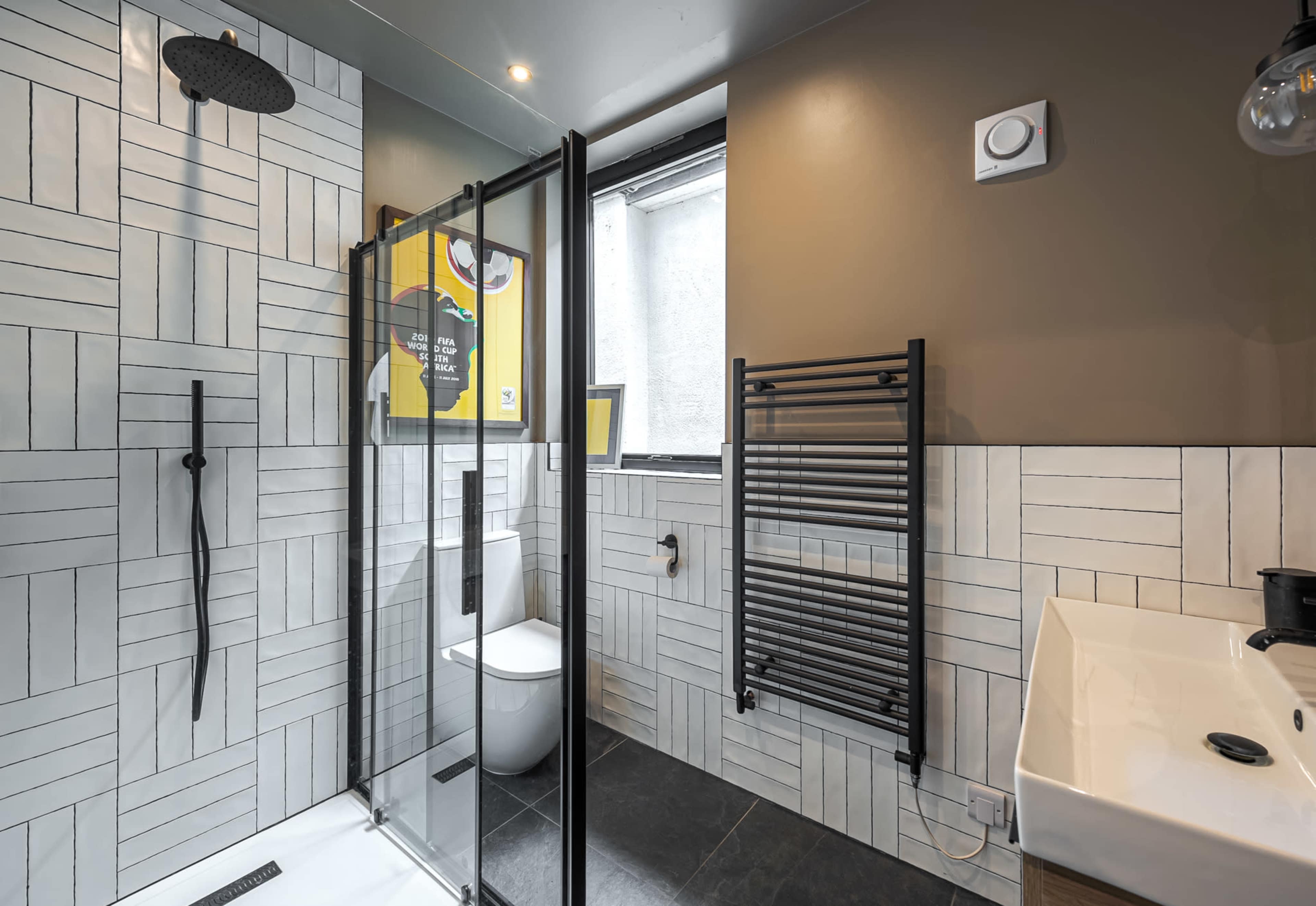 A modern bathroom featuring a glass shower enclosure, a toilet, a sink with a faucet, and tiled walls with a mix of horizontal and vertical patterns.