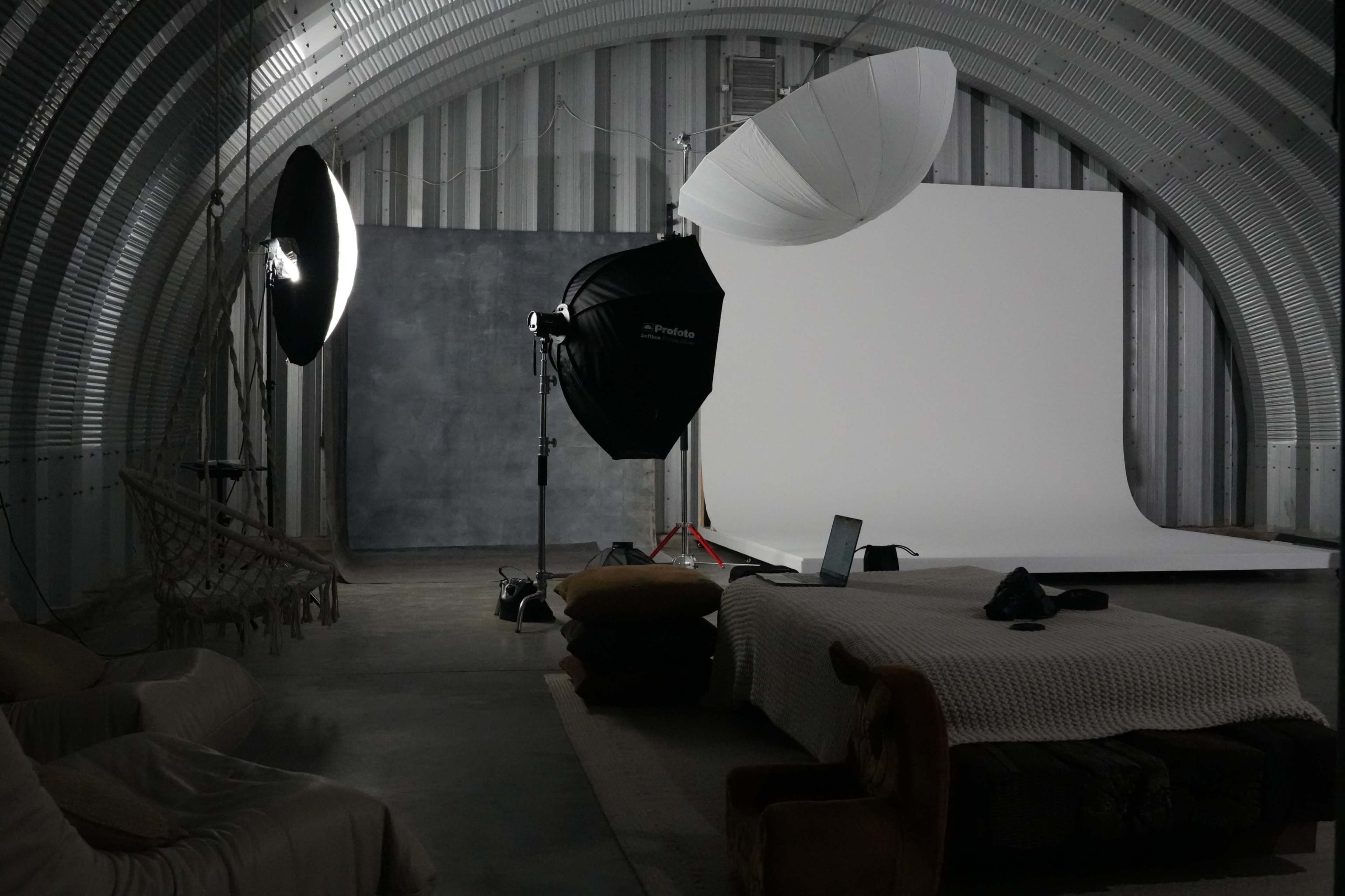 The image shows a photography studio with softbox lighting, a backdrop, and a seating area with furniture.