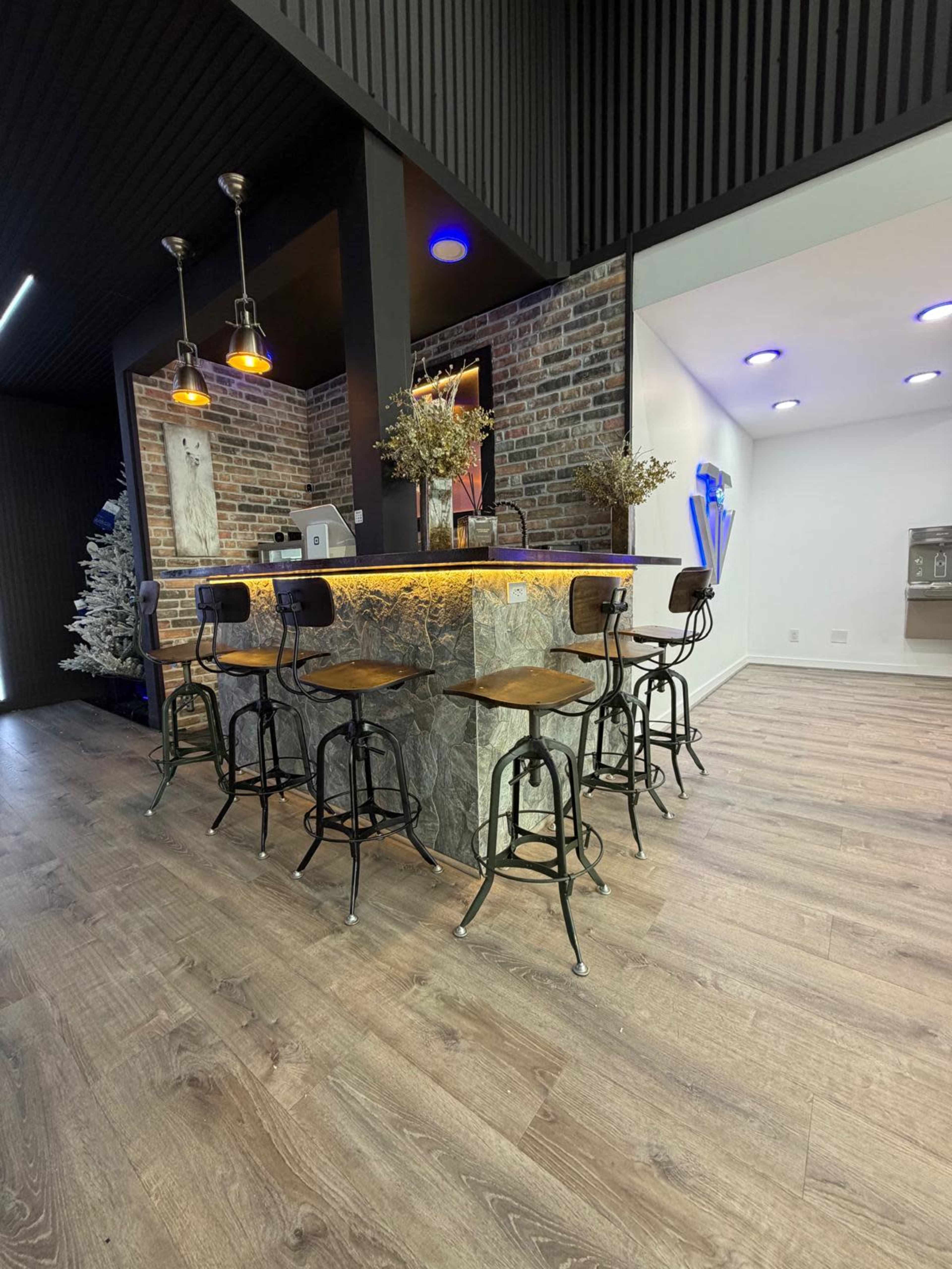 The image shows a modern bar area with a stone countertop and wooden stools, situated against a backdrop of exposed brick and minimalist decor.