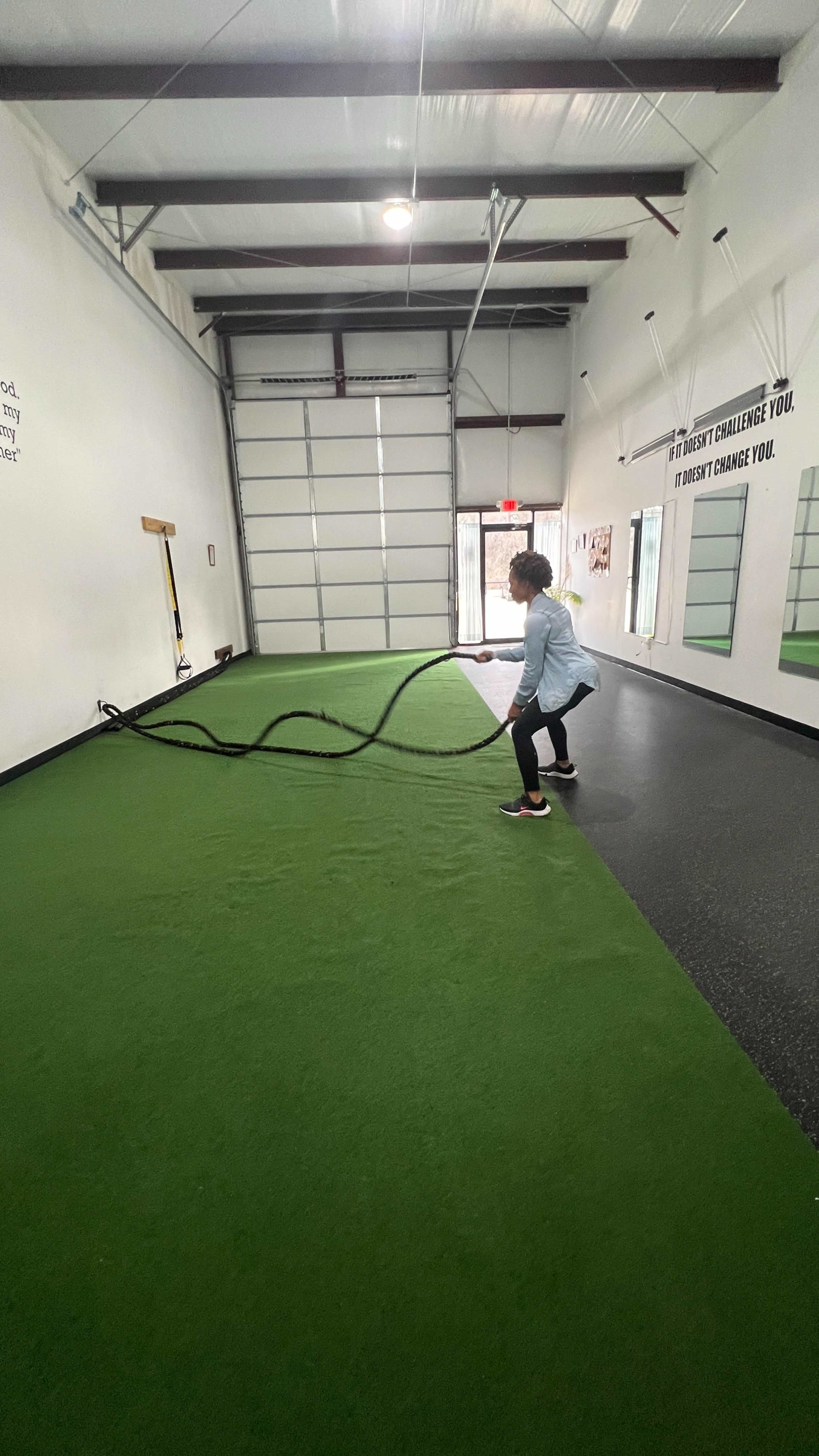 A person stands on a green gym floor, performing an exercise with heavy ropes in a spacious indoor training facility.