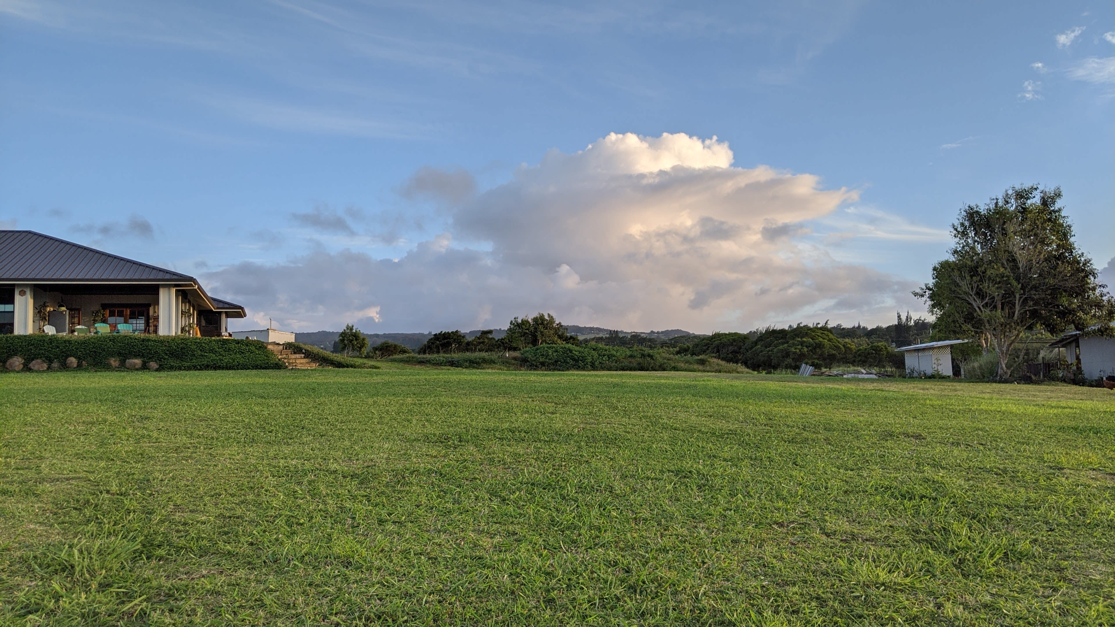 A house with a covered porch sits on a grassy field under a cloudy sky.