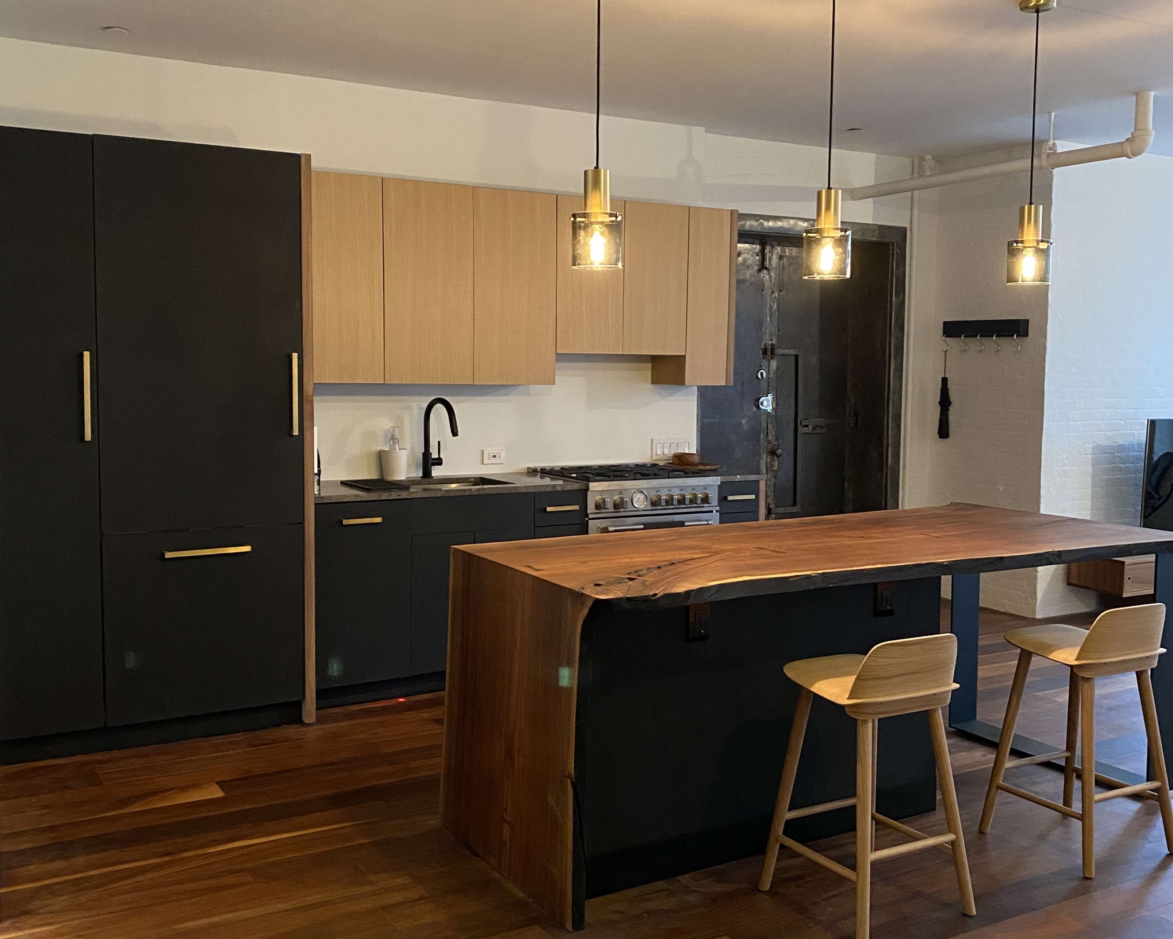 A modern kitchen with dark cabinetry, wood accents, a large wooden island, and pendant lights overhead.