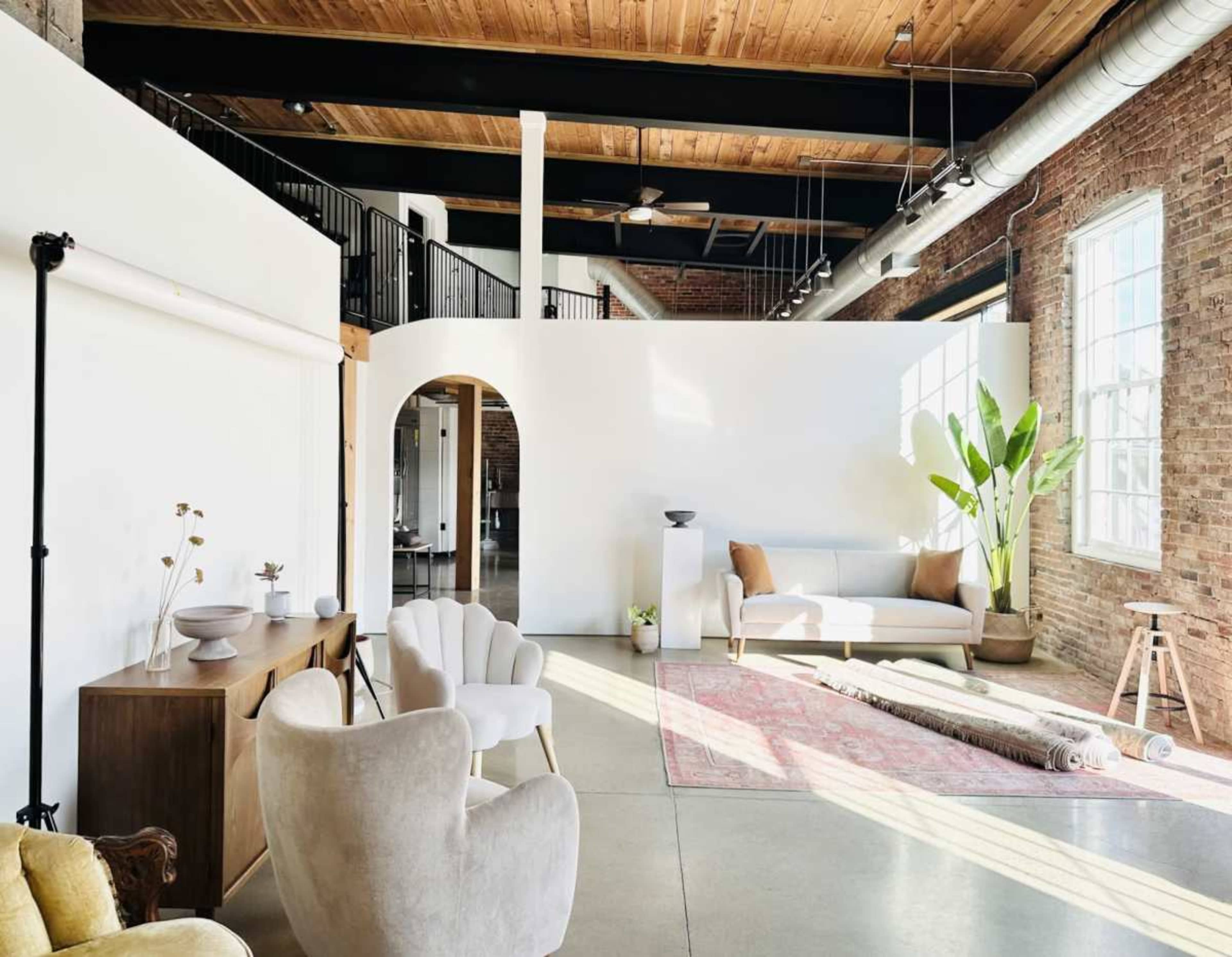 The image shows a spacious, contemporary living area with large windows, a light-colored sofa, and a potted plant, highlighting a mix of natural materials and textures.