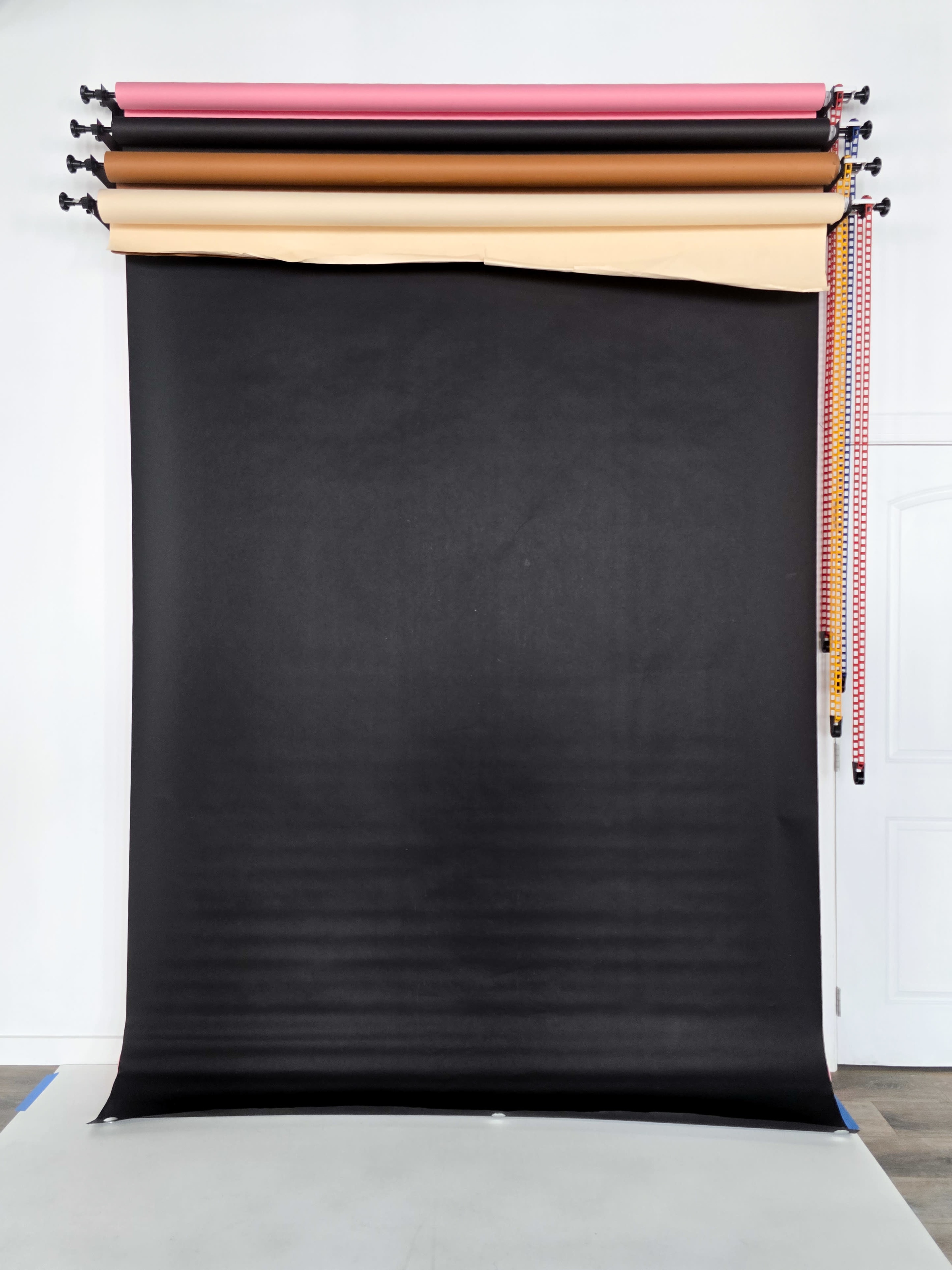 A black backdrop is hung in front of a wall, with rolls of colored paper resting on top.