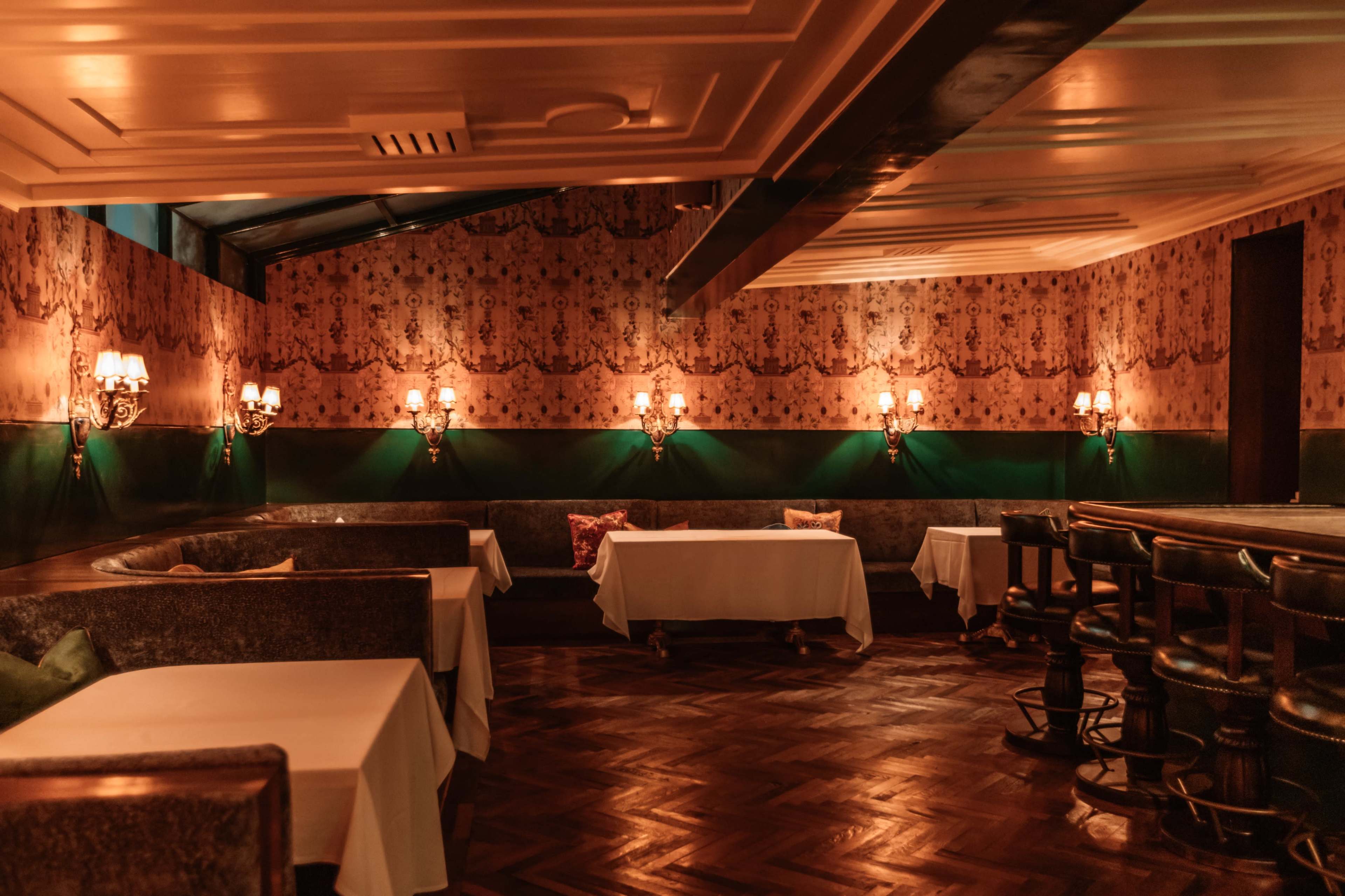 The image shows a dimly lit restaurant interior featuring tables with white tablecloths, plush seating along the walls, and elegant wall sconces.