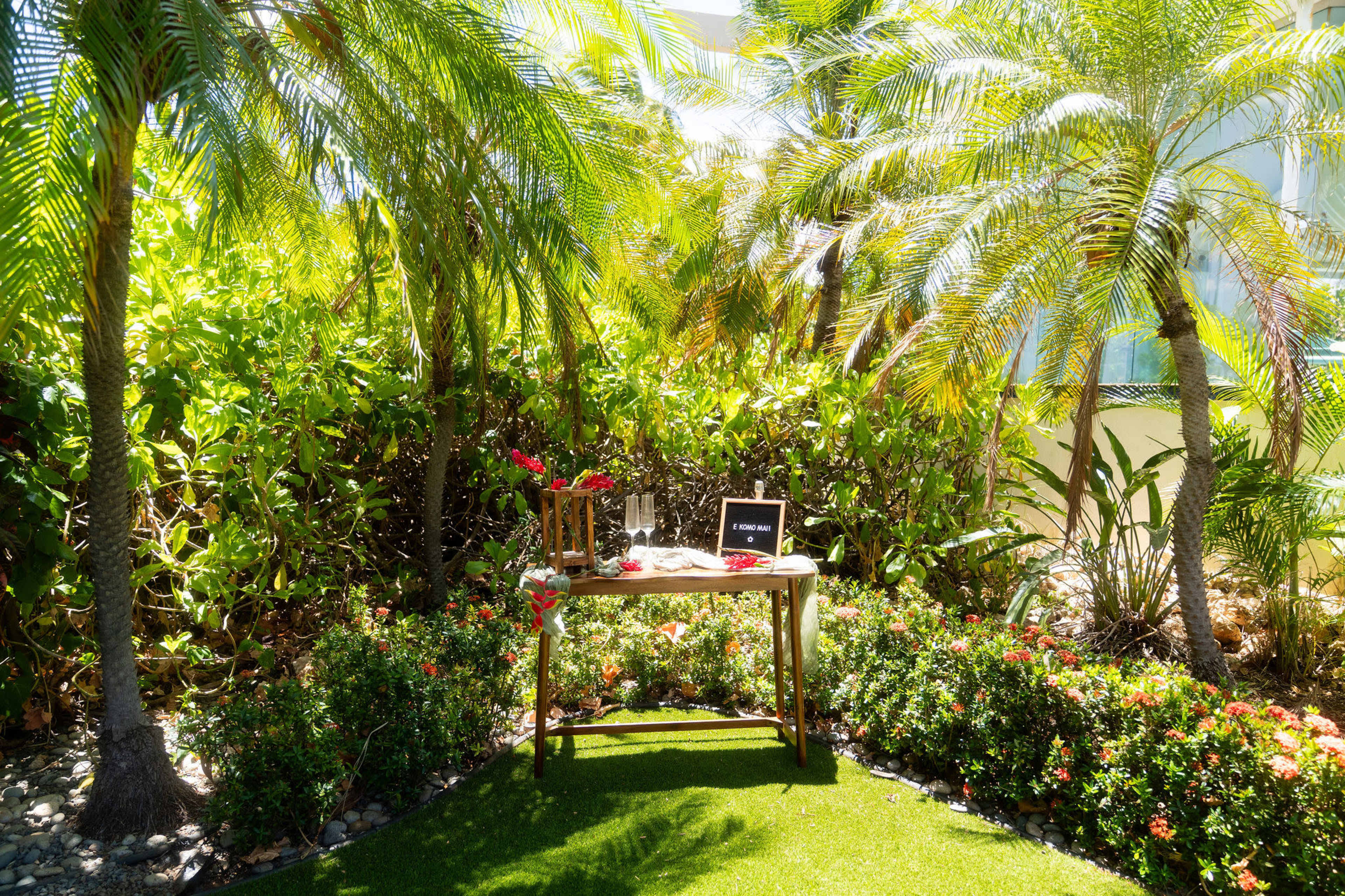 A small wooden table adorned with flowers sits surrounded by lush greenery and palm trees.