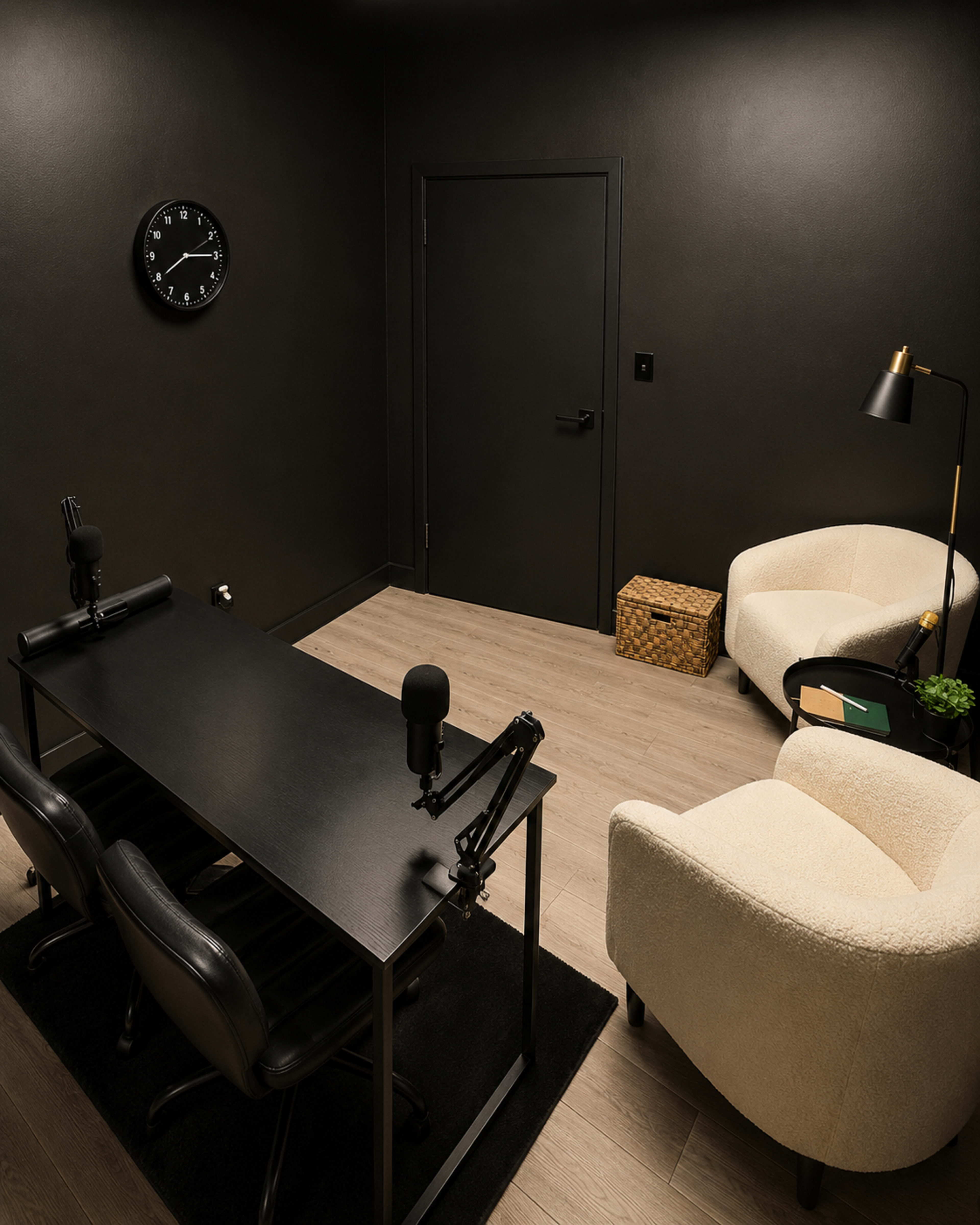 The image shows a dimly lit, modern recording studio with a black table, two chairs, and a cream-colored armchair in a corner.