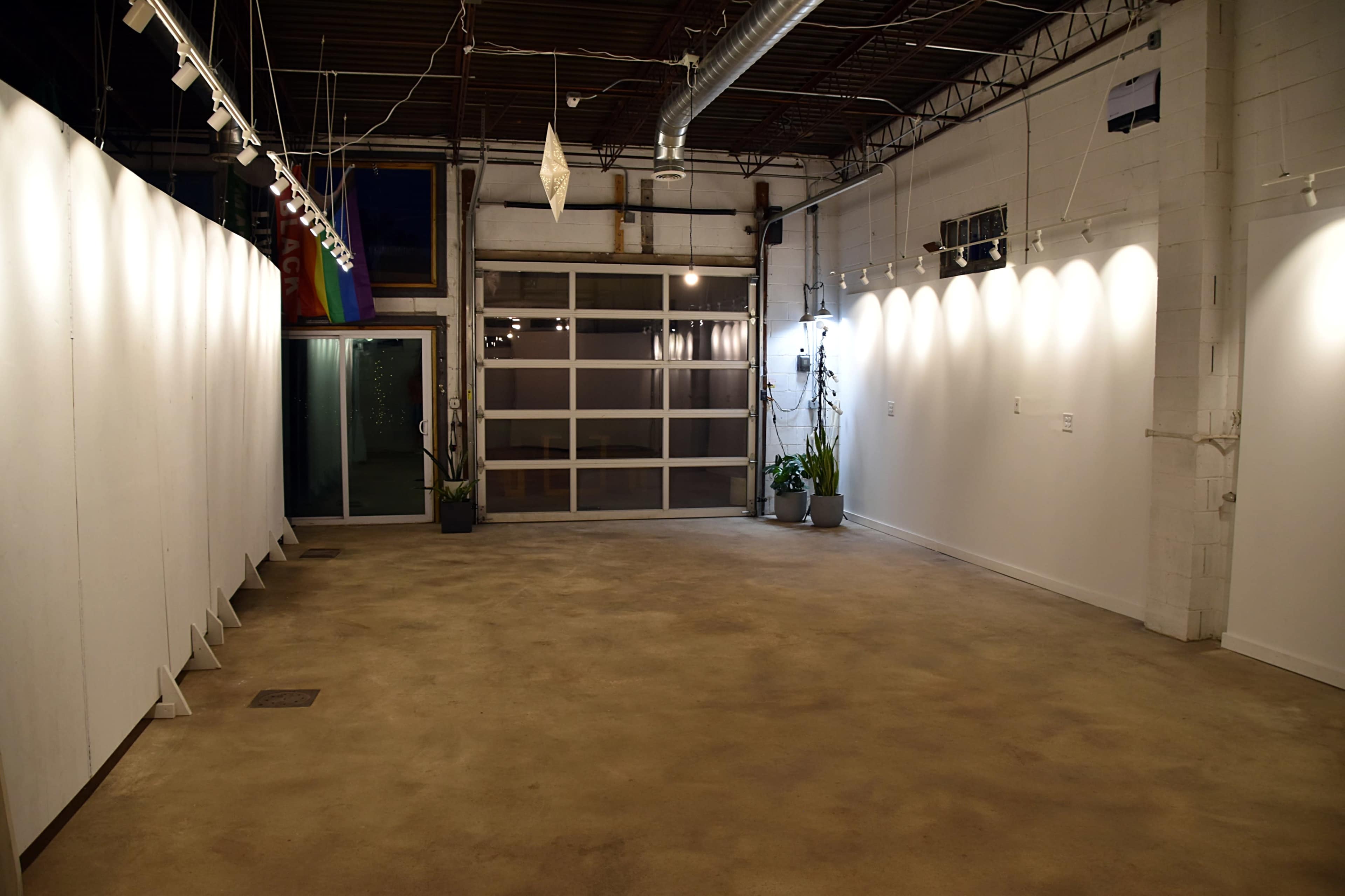 An empty art gallery space with white walls and a concrete floor, illuminated by overhead lights.