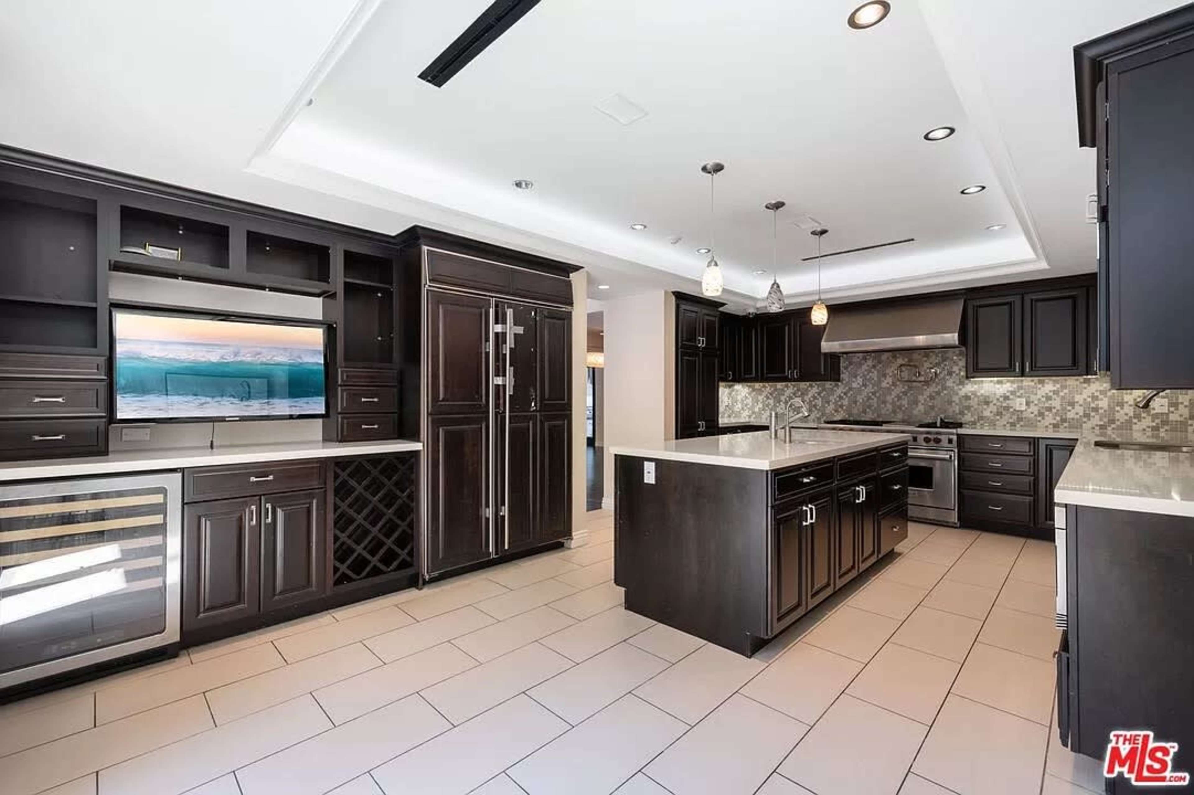 A modern kitchen featuring dark cabinetry, stainless steel appliances, and a spacious layout with a large island.
