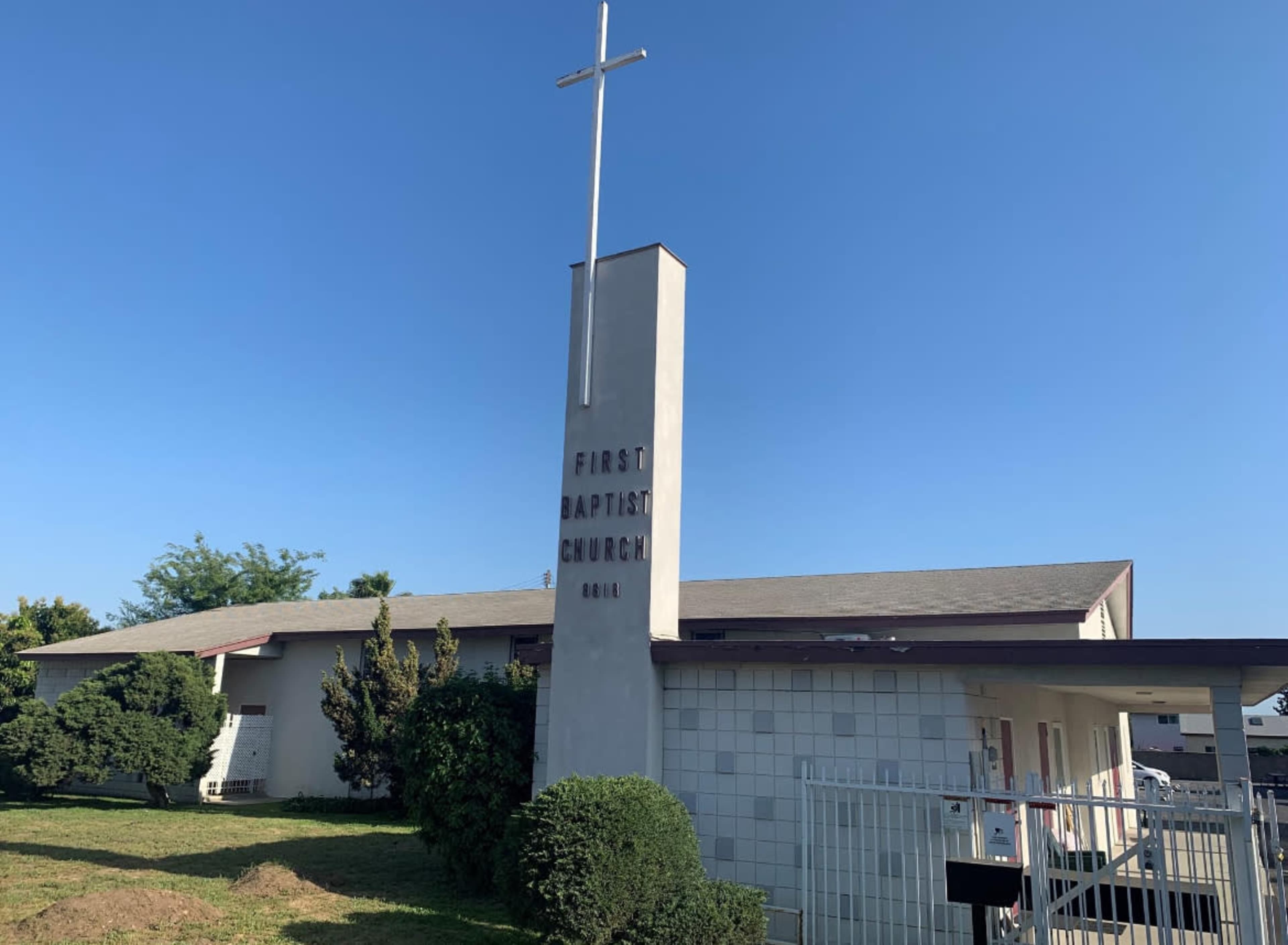 The exterior of the First Baptist Church, featuring a prominent cross on a tall structure and a simple building design.