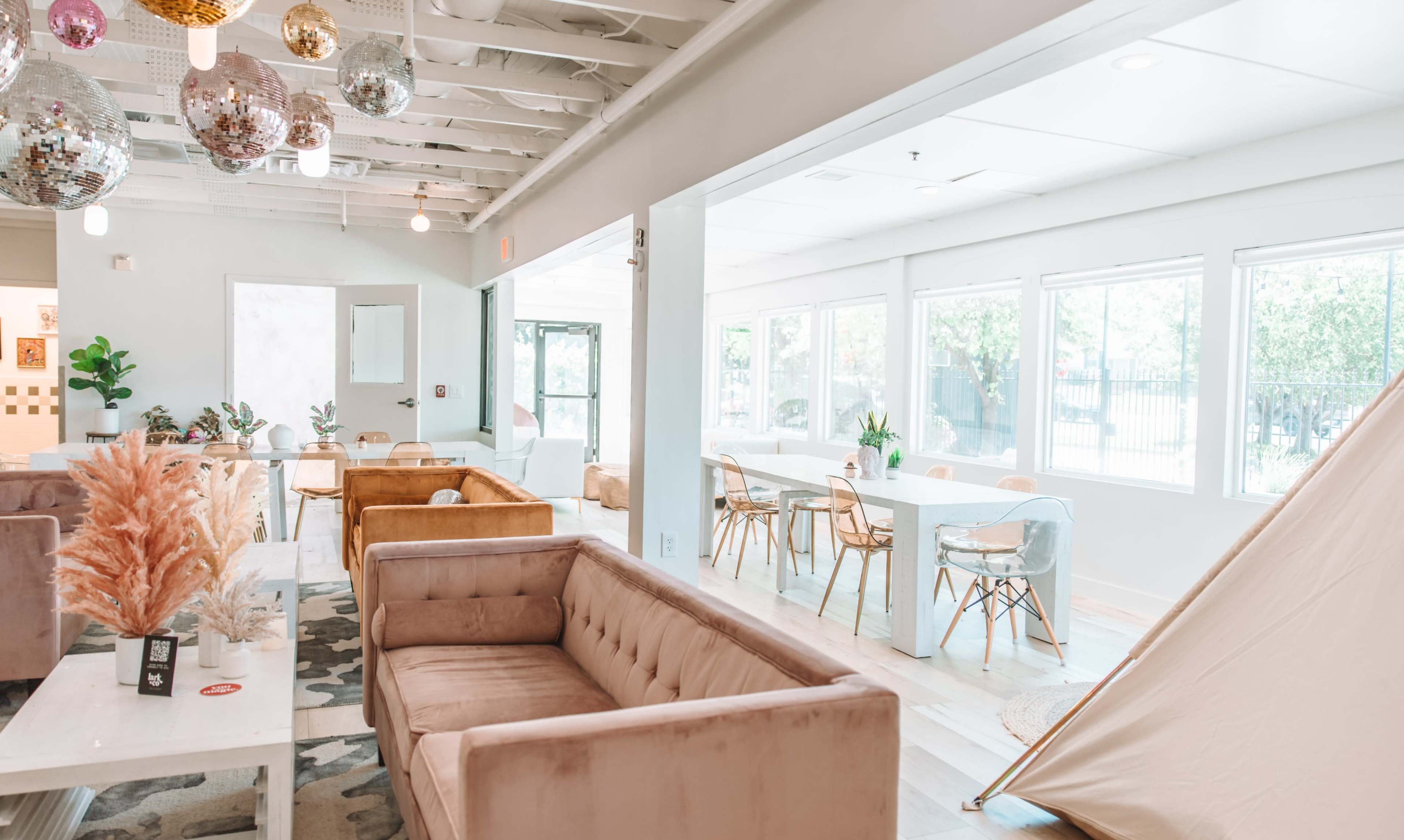 A modern lounge area with plush couches, a dining space featuring clear chairs and a table, and light streaming through large windows.