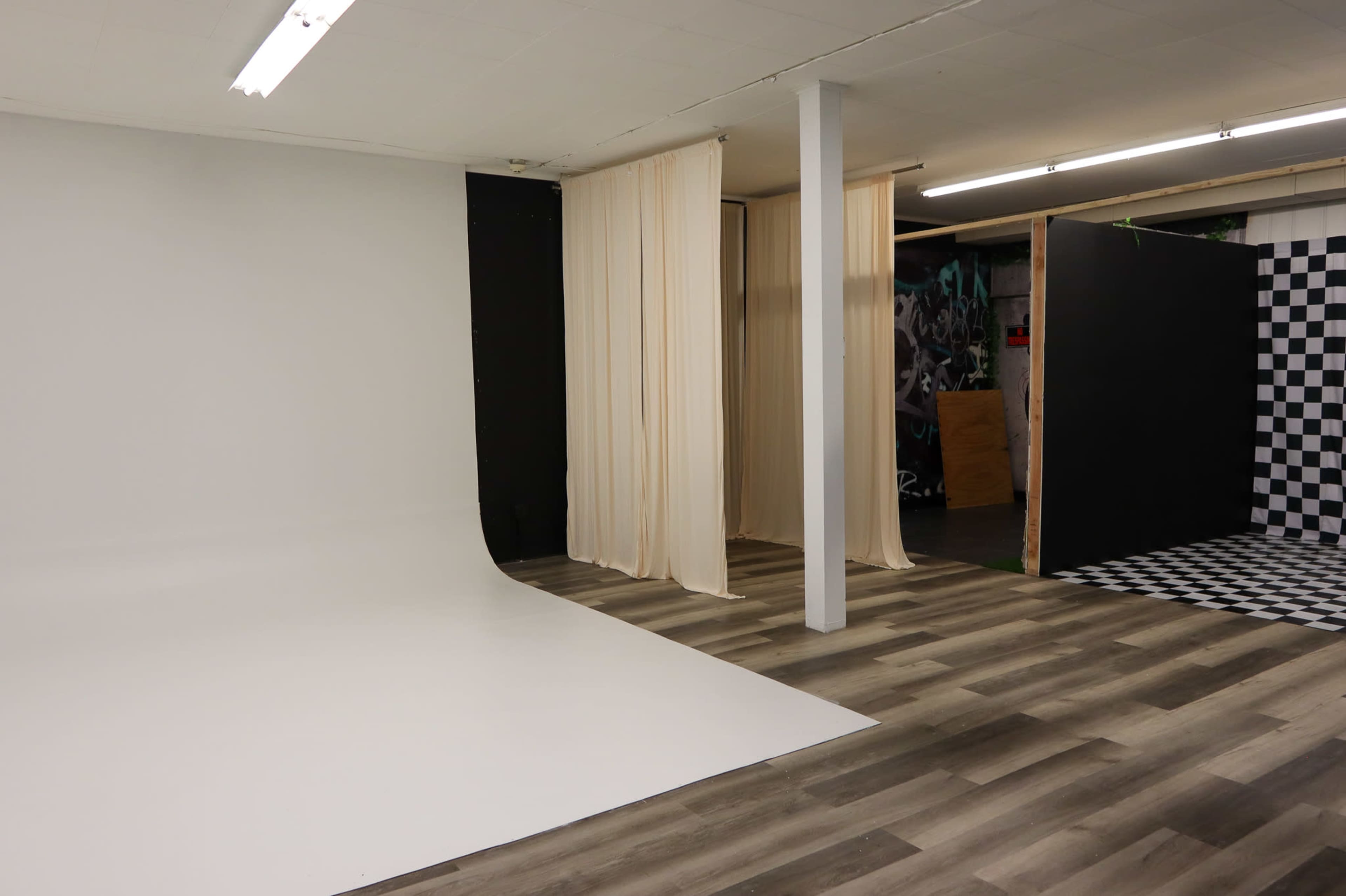A spacious photo studio featuring a white backdrop, draped curtains, and a checkered black-and-white wall.