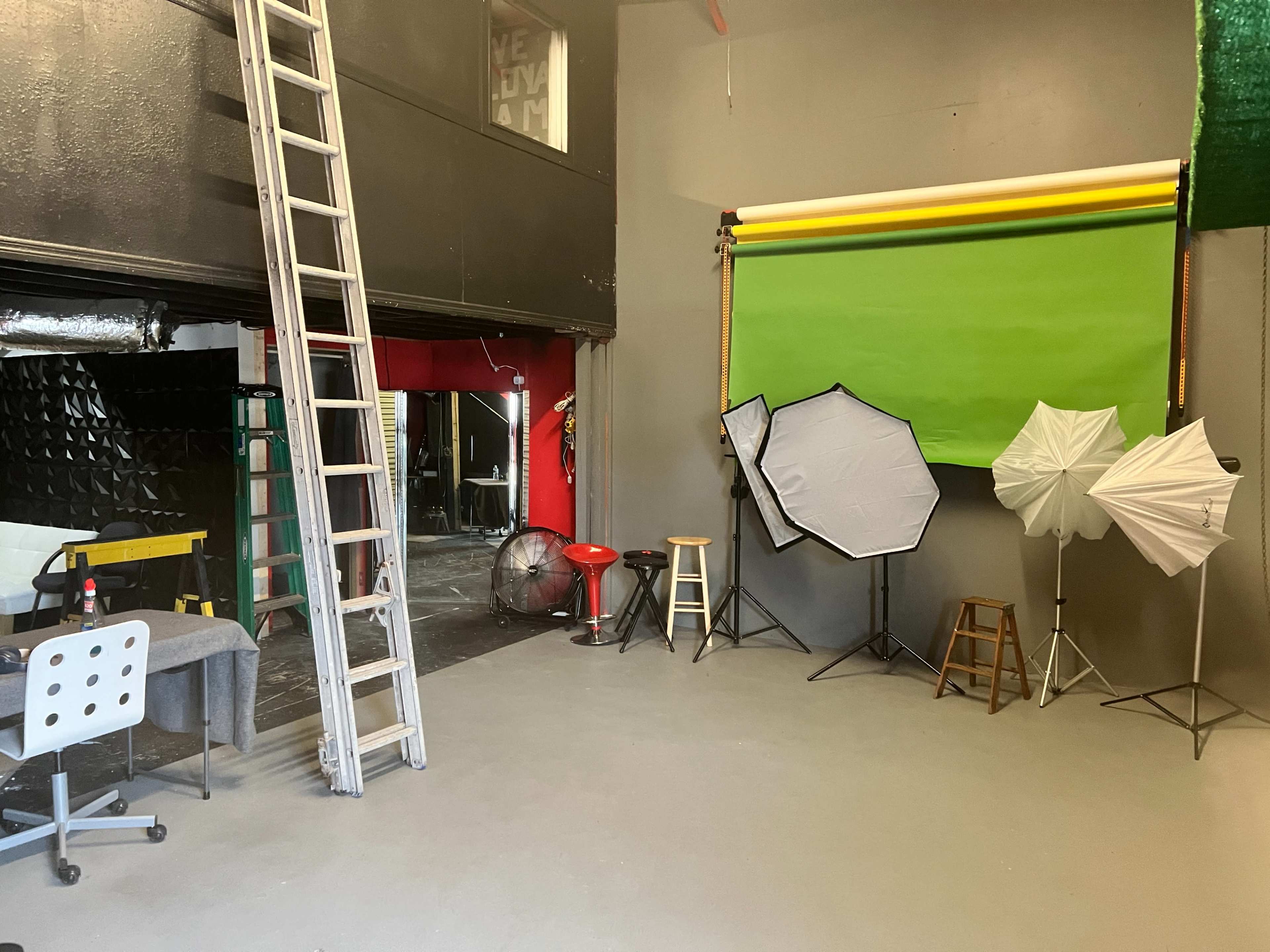 A photography studio with various lighting equipment, backdrops, a ladder, and a workspace area.