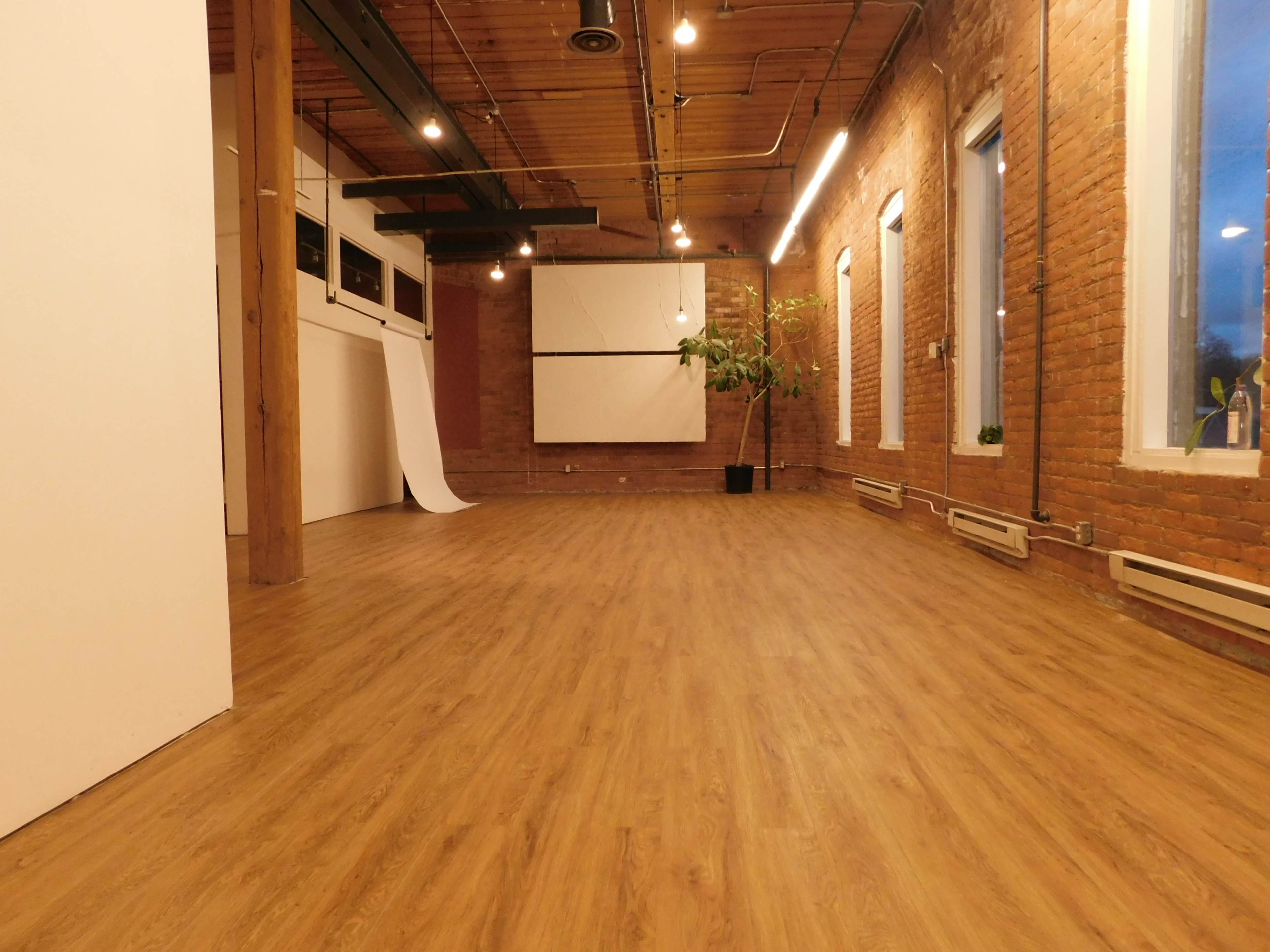 A large, empty room with wooden flooring, exposed brick walls, and a projector screen on one wall.