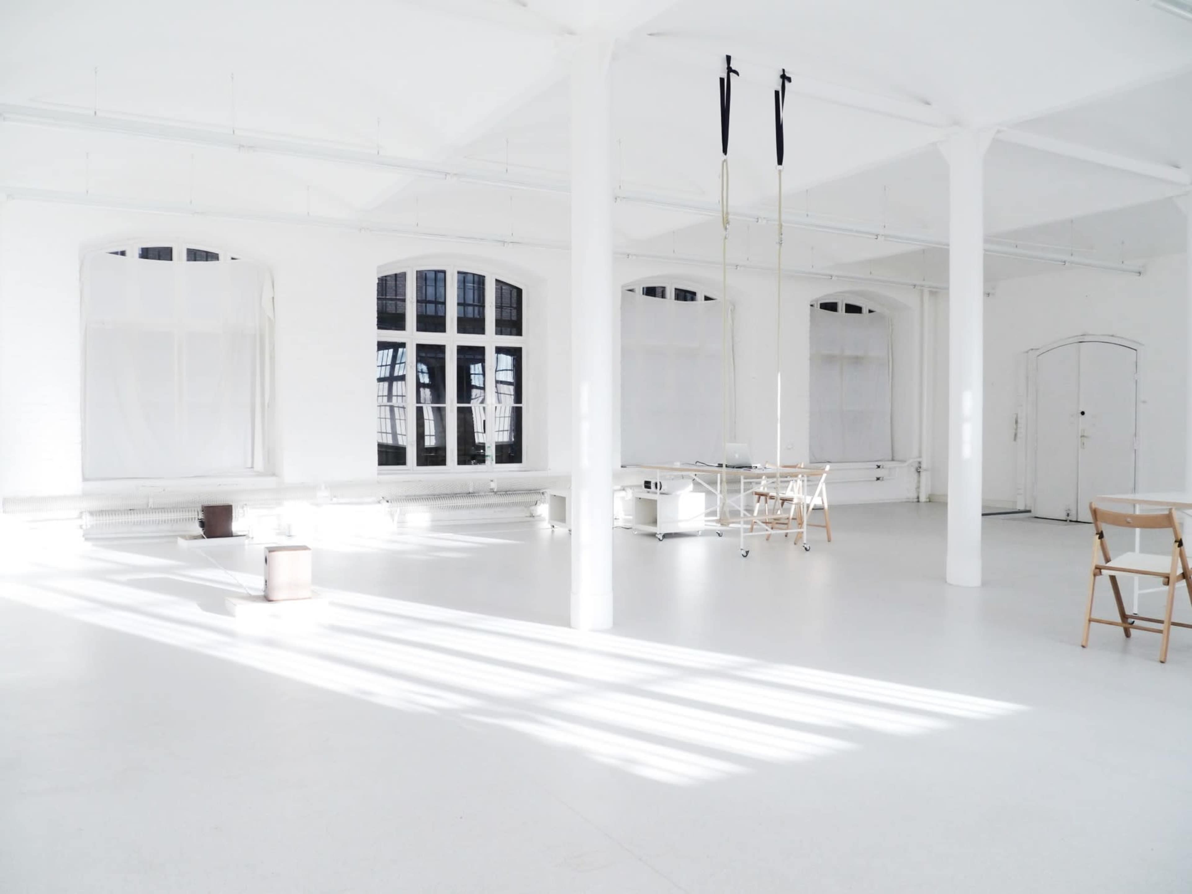 A spacious, empty white room with large windows and minimalist decor.