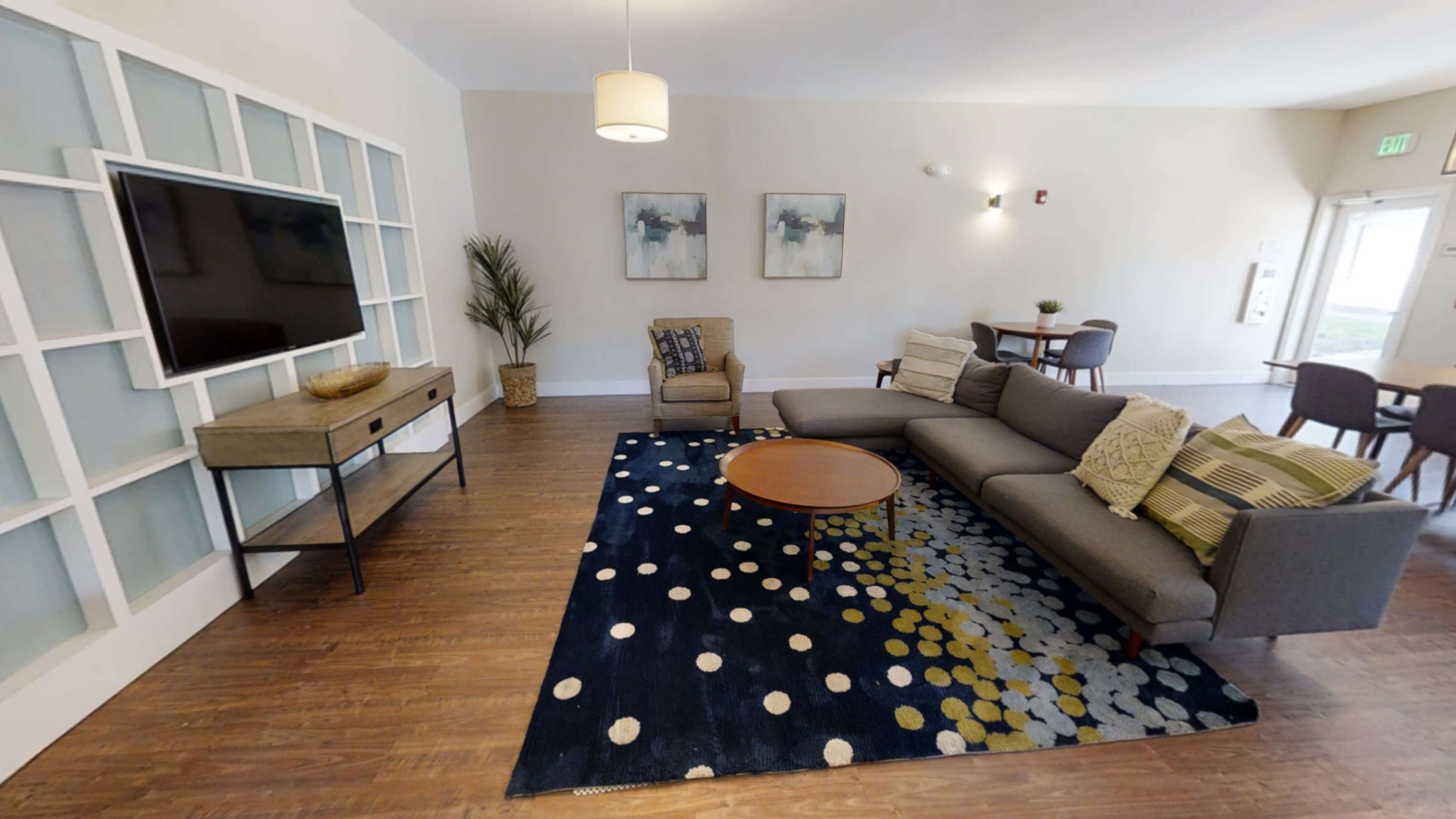 The living area features a sectional sofa, a mid-century modern coffee table, a large TV on a wall-mounted shelf, and a dining area in the background.