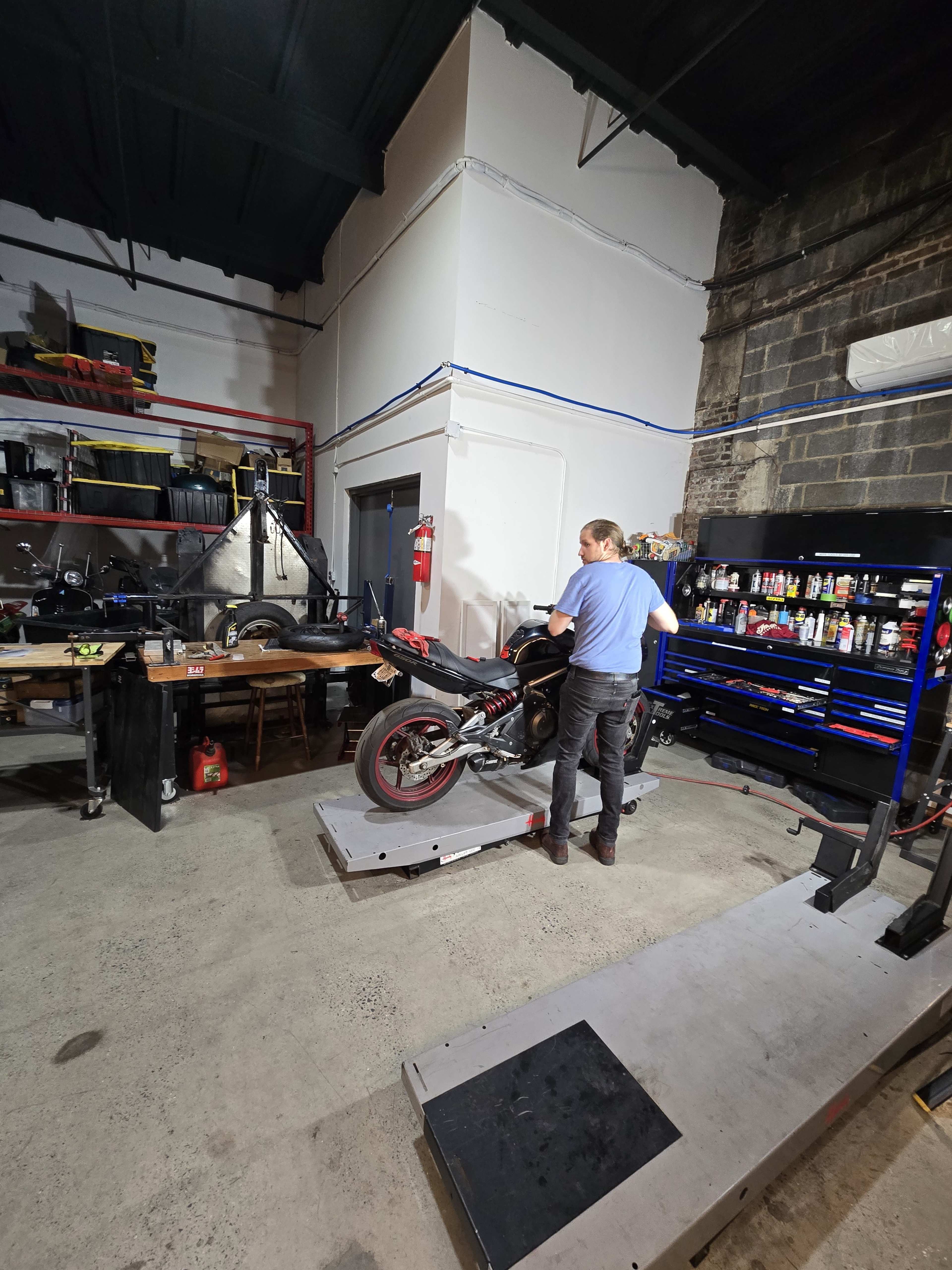 A person is working on a motorcycle in a garage filled with tools and equipment.