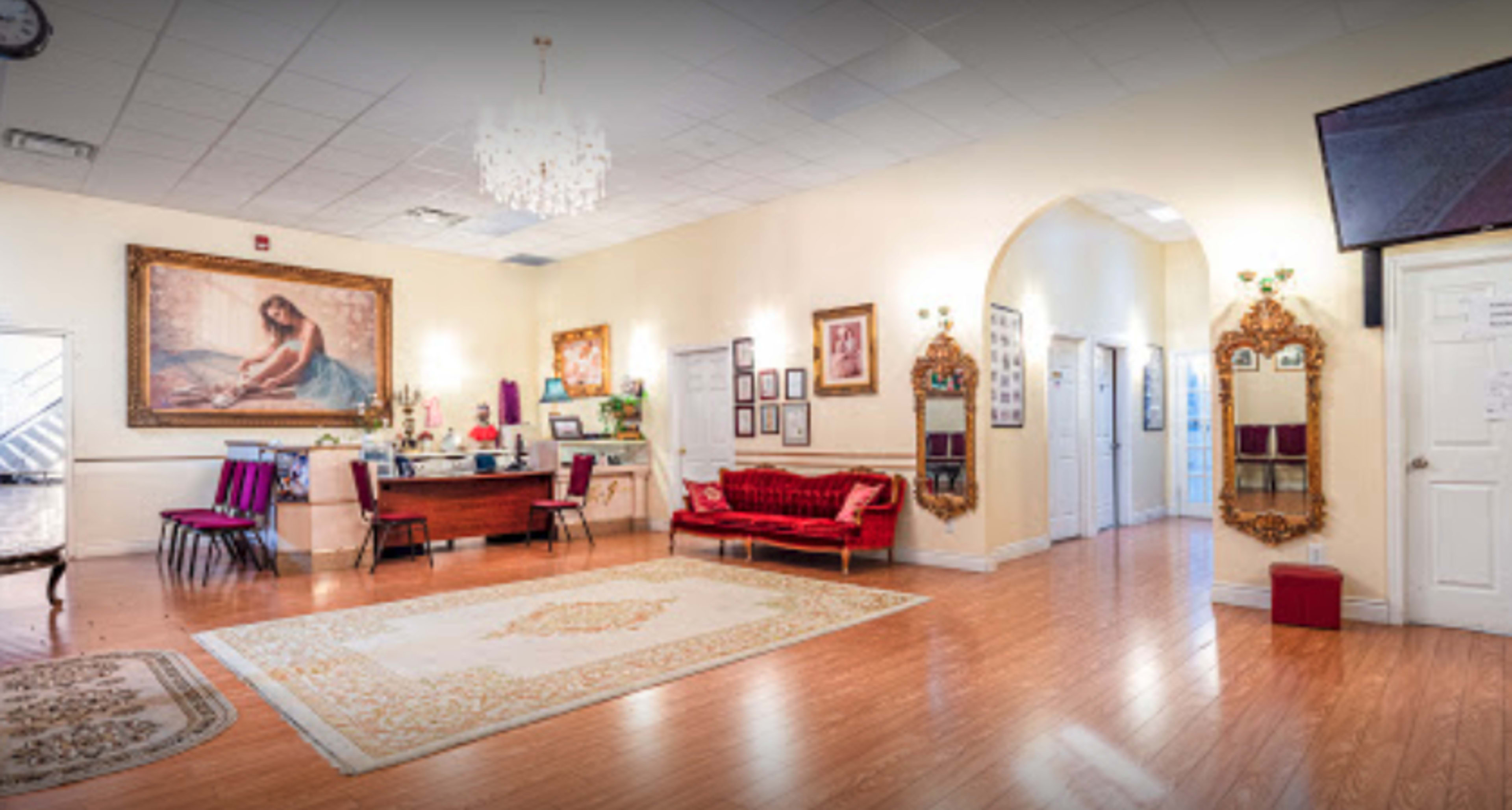 A spacious reception area with wooden flooring, a large painting on the wall, a red velvet couch, and a decorative chandelier.