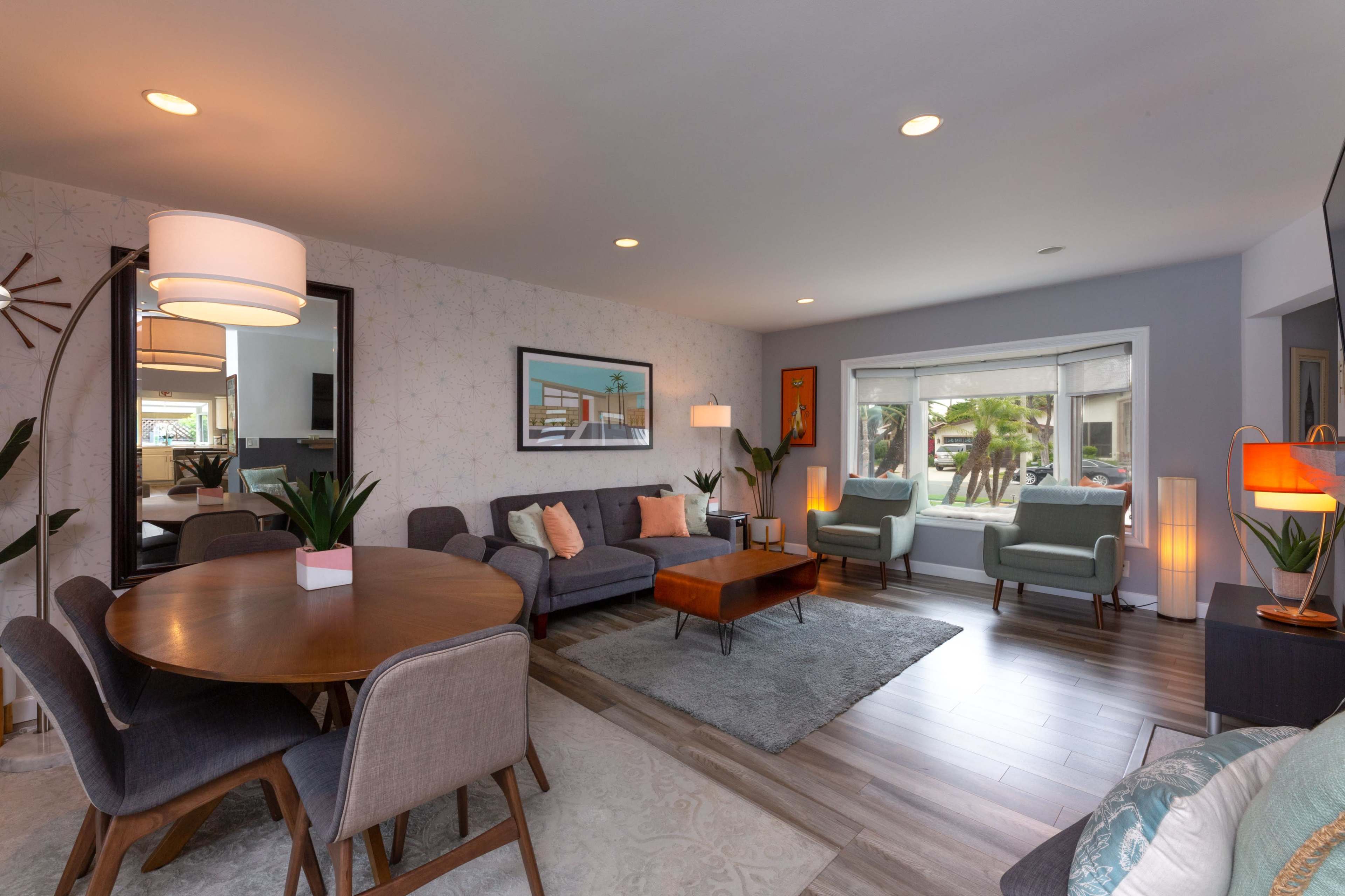 A modern living room with a seating area, a round dining table, and large windows overlooking palm trees.