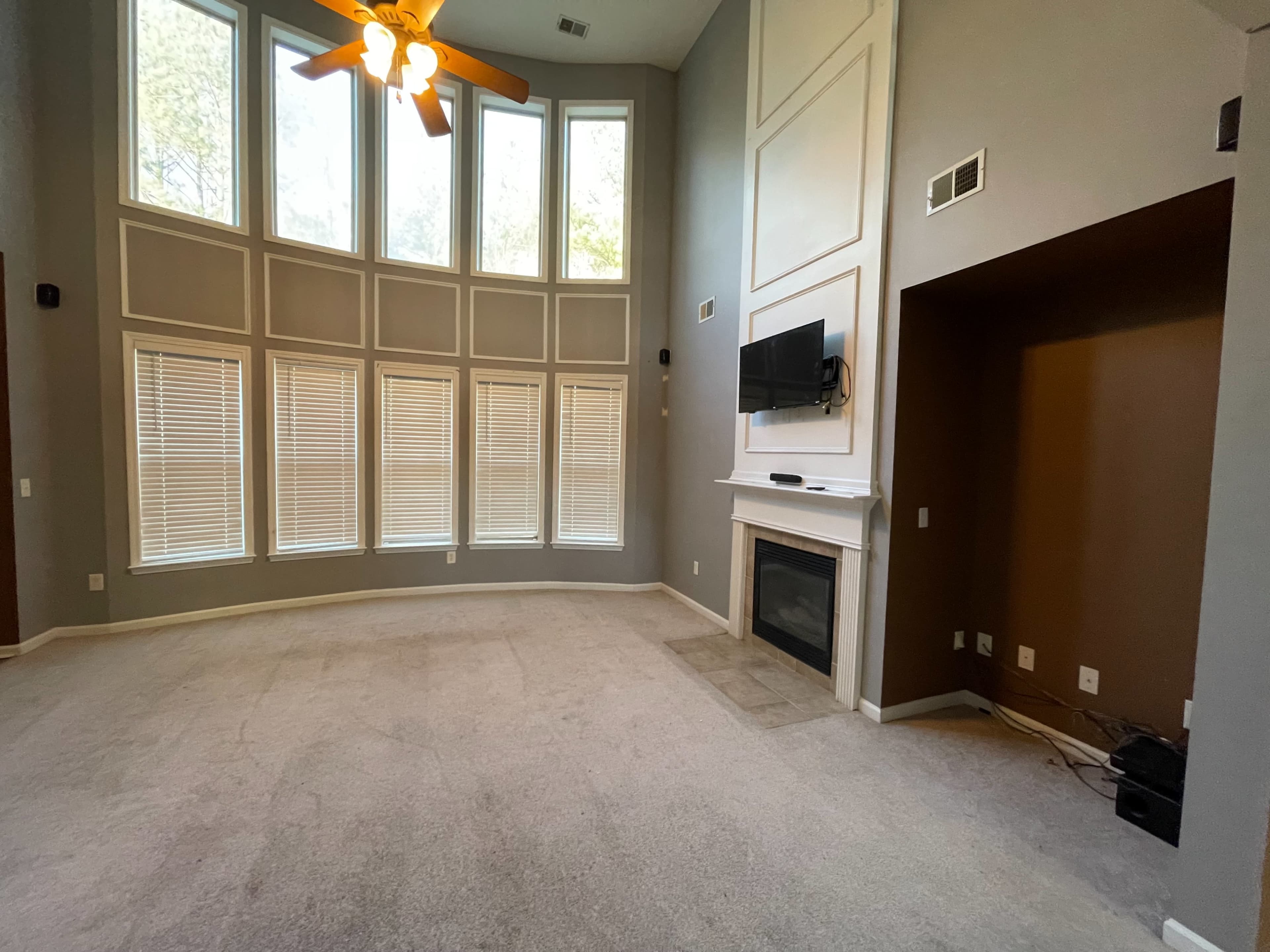 A spacious living room with large windows, a fireplace, and a mounted television on a light-colored wall.