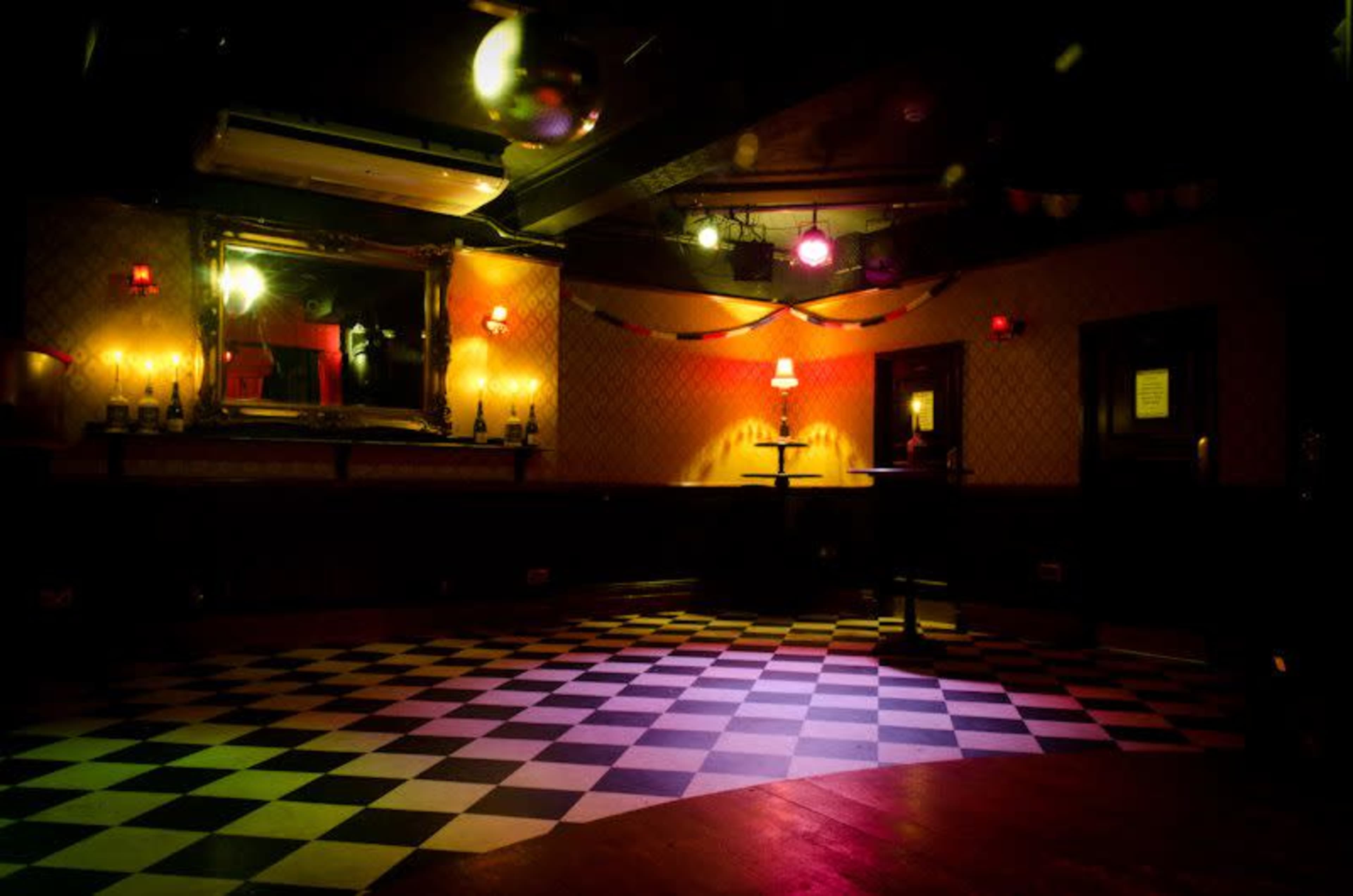 The scene depicts a dimly lit room with a checkered floor, decorated with colorful lights and a large mirror.