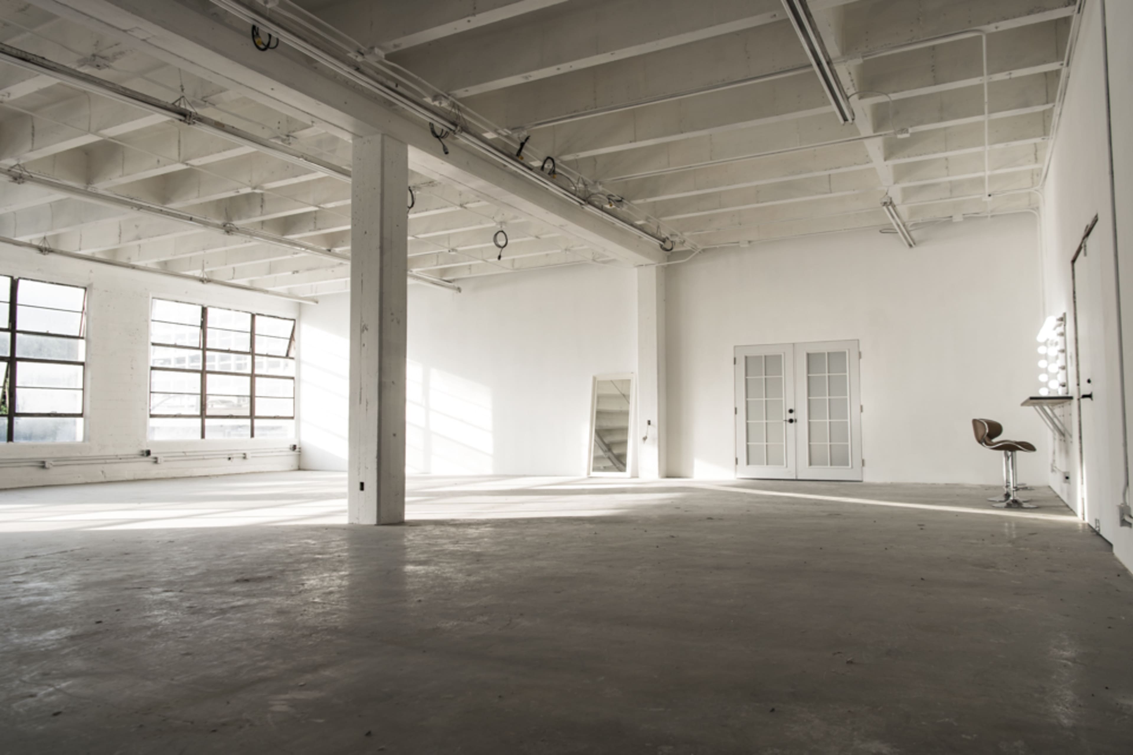 A spacious, empty room with high ceilings, large windows, and minimal furnishings.