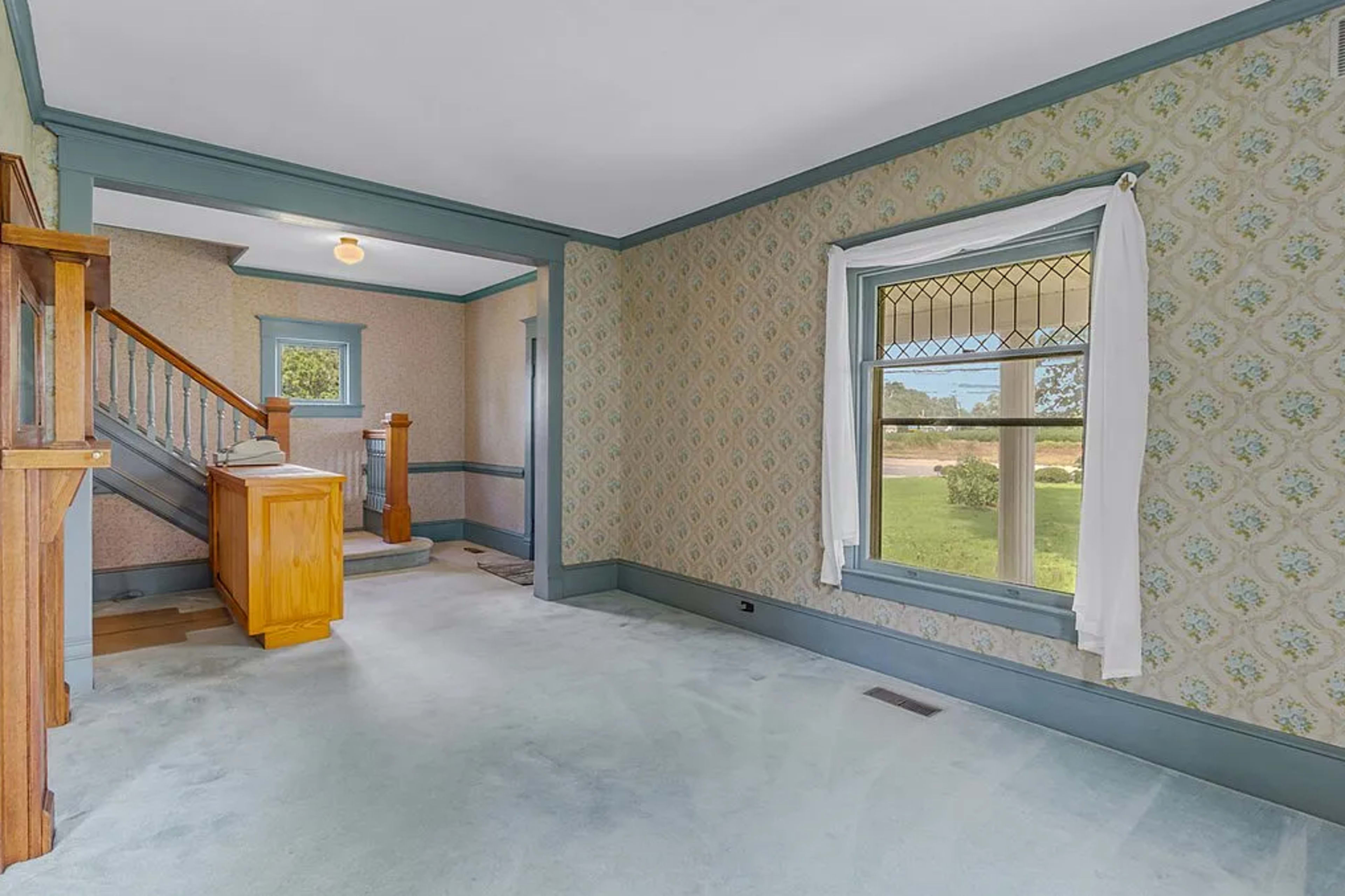 The image shows a spacious foyer with light blue carpeting, patterned wallpaper, and a staircase leading to an upper level.