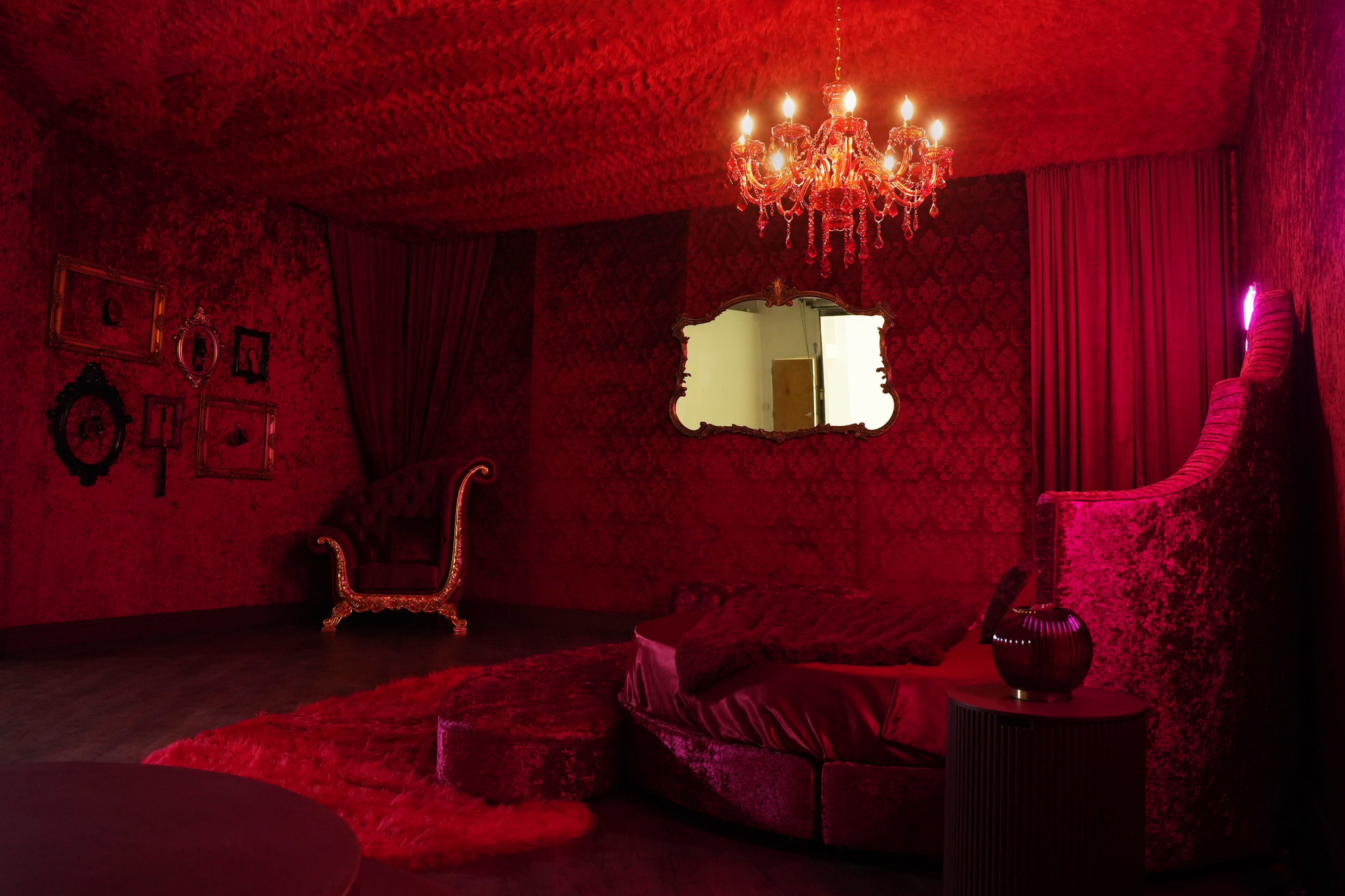 The room features red velvet walls, a chandelier, a large bed, and ornate furniture.