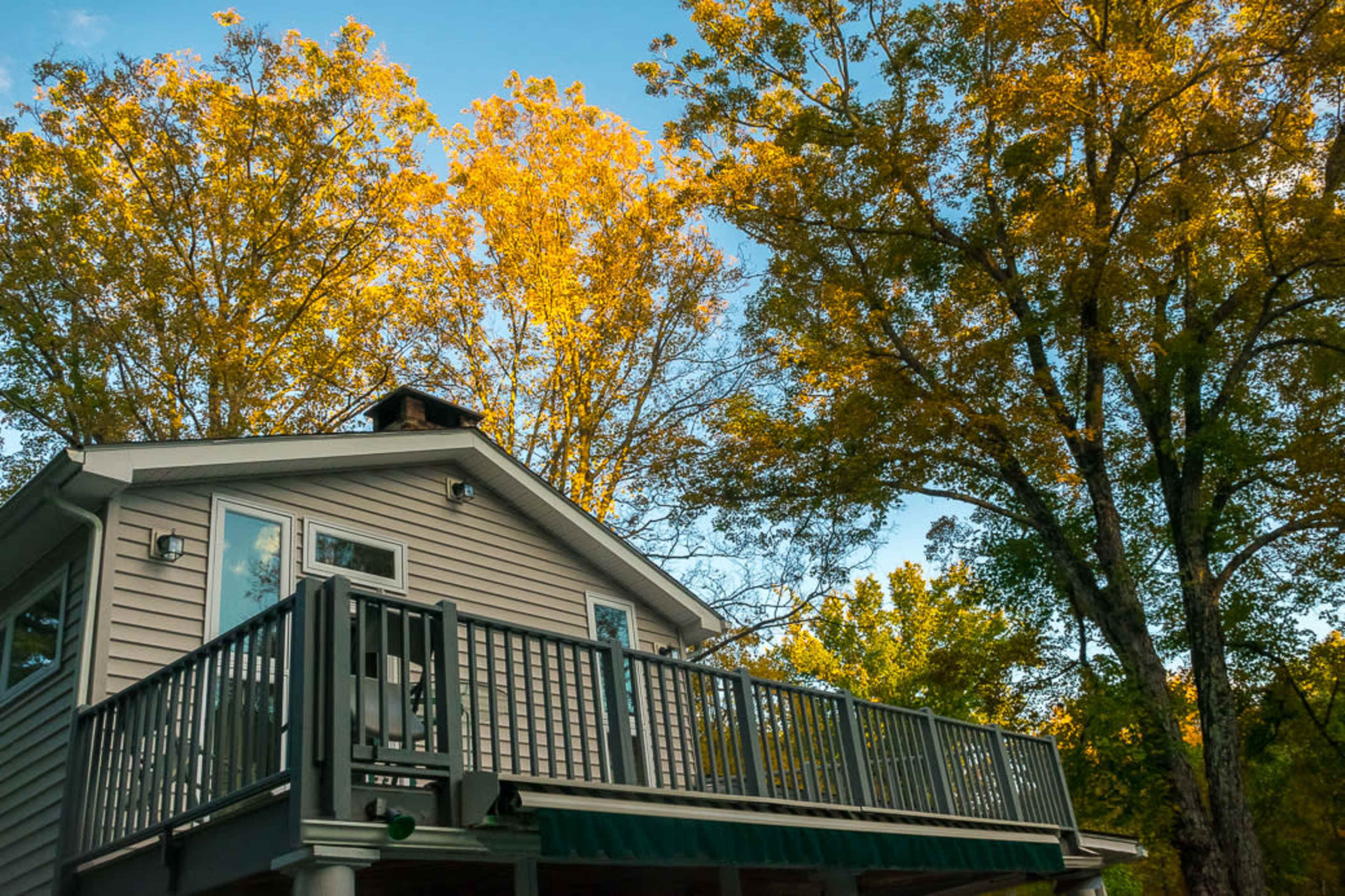 A two-story house with a balcony is surrounded by tall trees with bright yellow leaves.