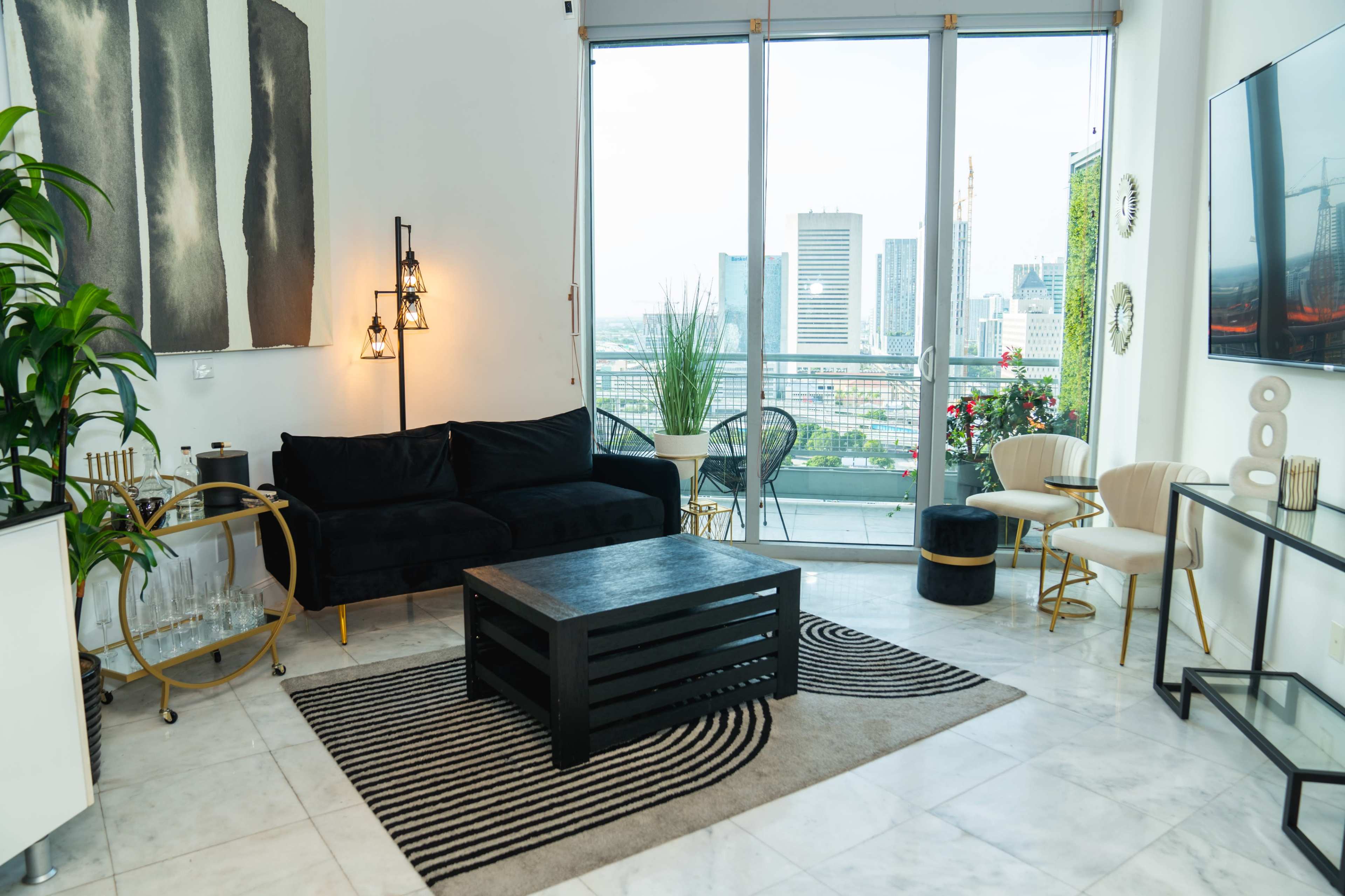 A modern living room features a black sofa, a coffee table, and a large window with city views.