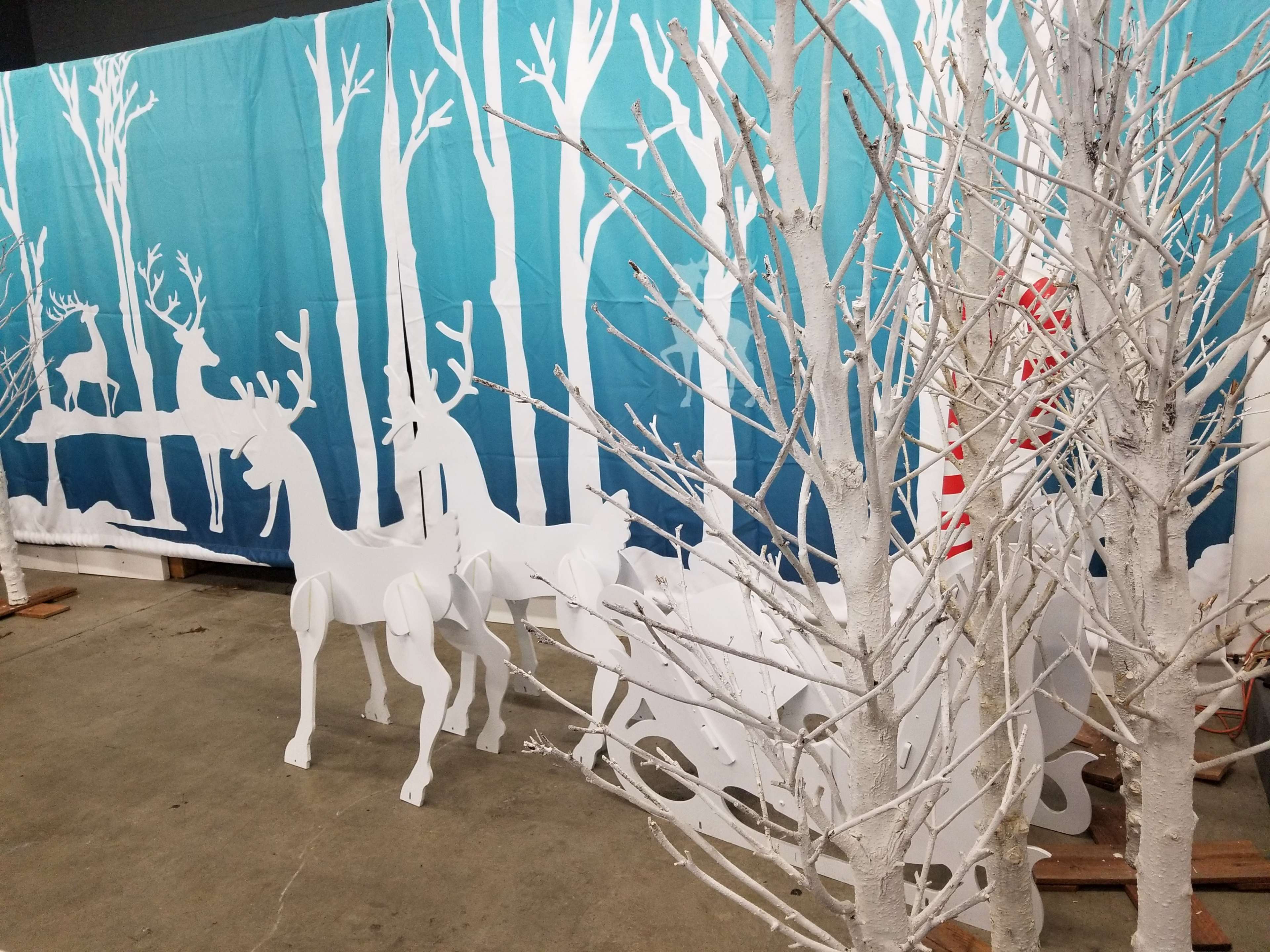 The scene features white silhouette reindeer and a sleigh set against a backdrop of teal fabric with white tree designs.