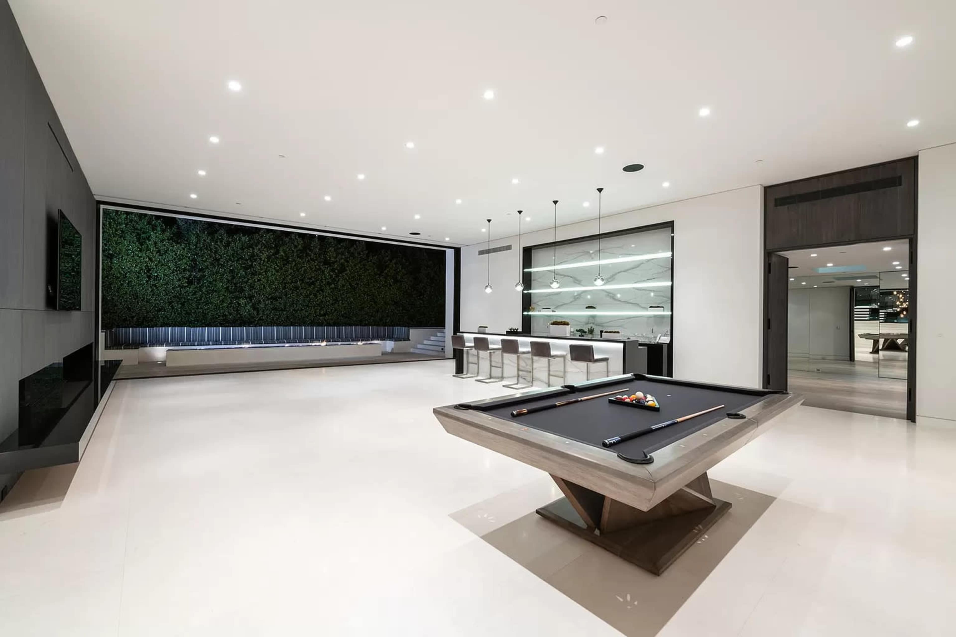 A modern living space features a pool table at its center, surrounded by sleek furnishings and a vertical garden on one wall.