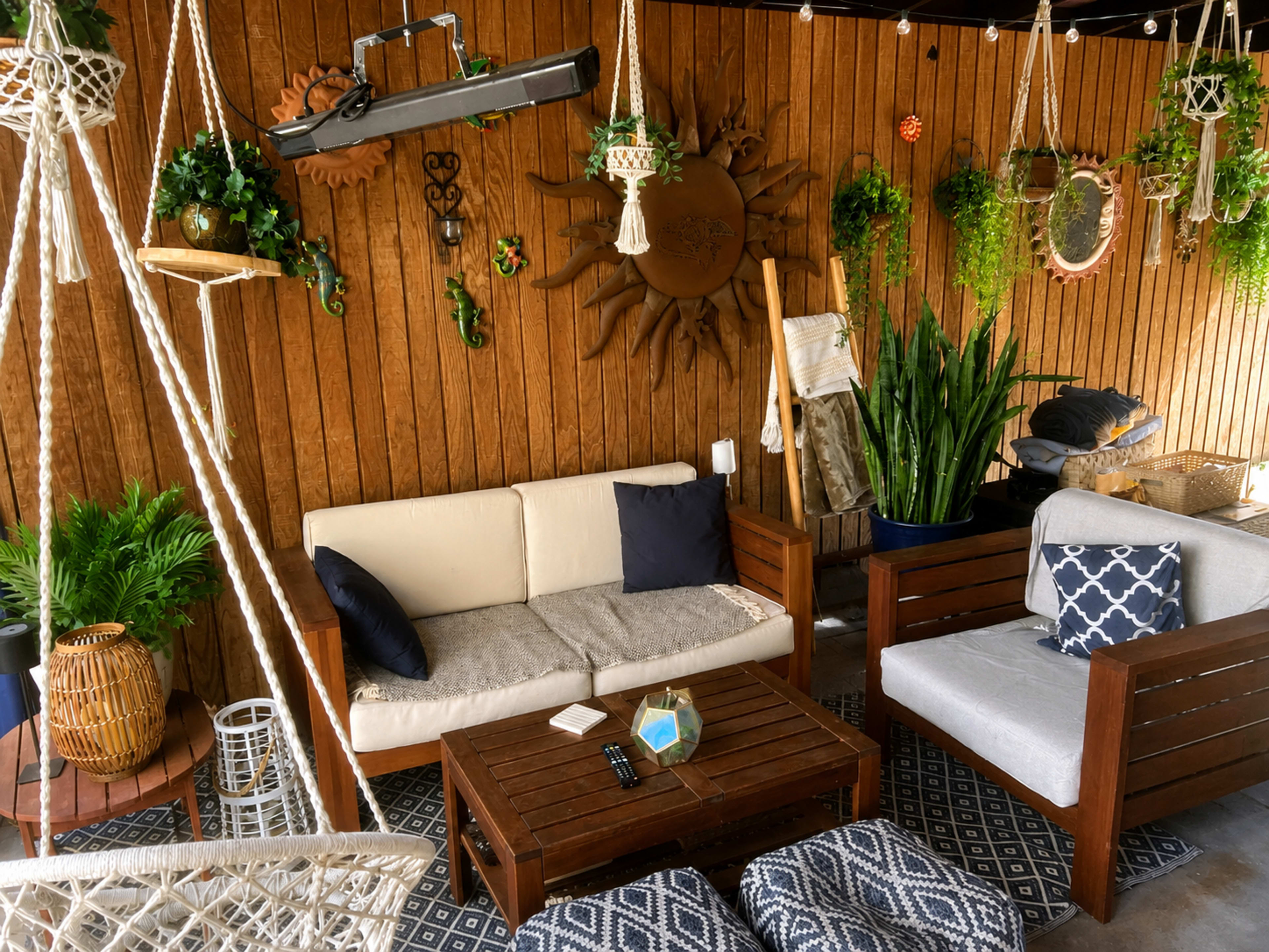 The image shows a cozy outdoor seating area featuring wooden furniture, hanging plants, and a textured wall made of wooden panels.
